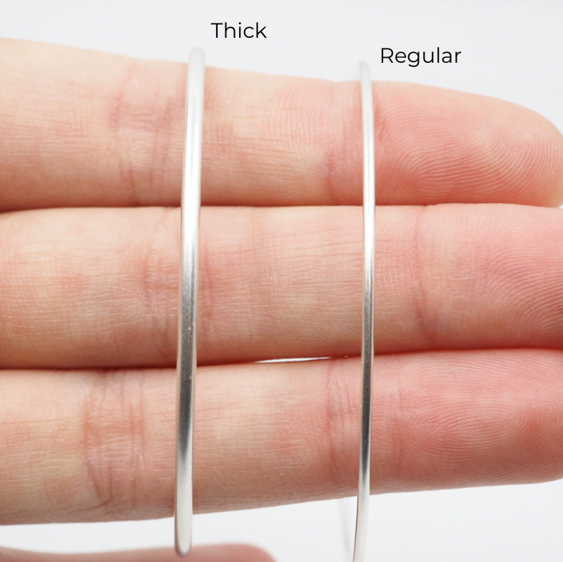 Two silver hoop earrings, one thick and one regular, on a hand against a white background.