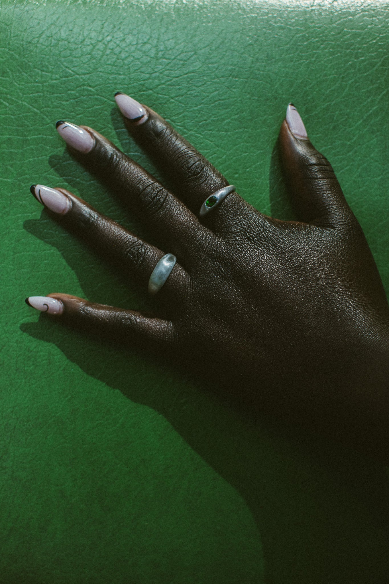 A close-up of a hand wearing two silver rings against a textured green background.