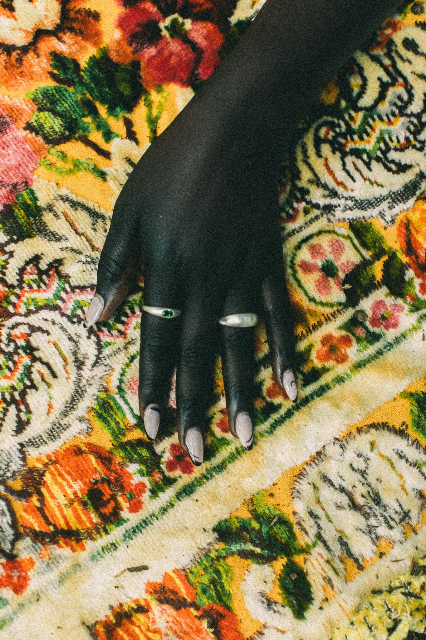 A close-up of a hand with silver rings, resting on a highly patterned, colorful woven rug.