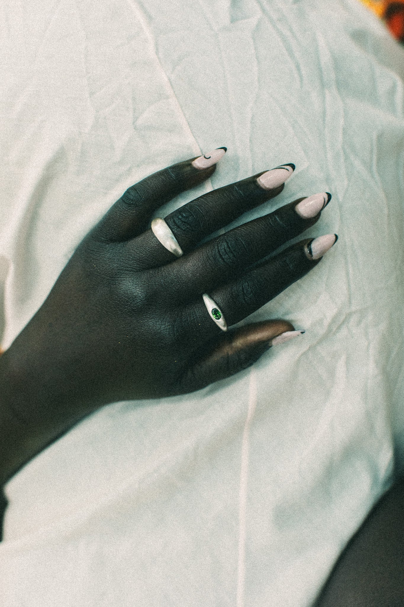 A close-up of a hand resting on a wrinkled white fabric, wearing two silver rings.