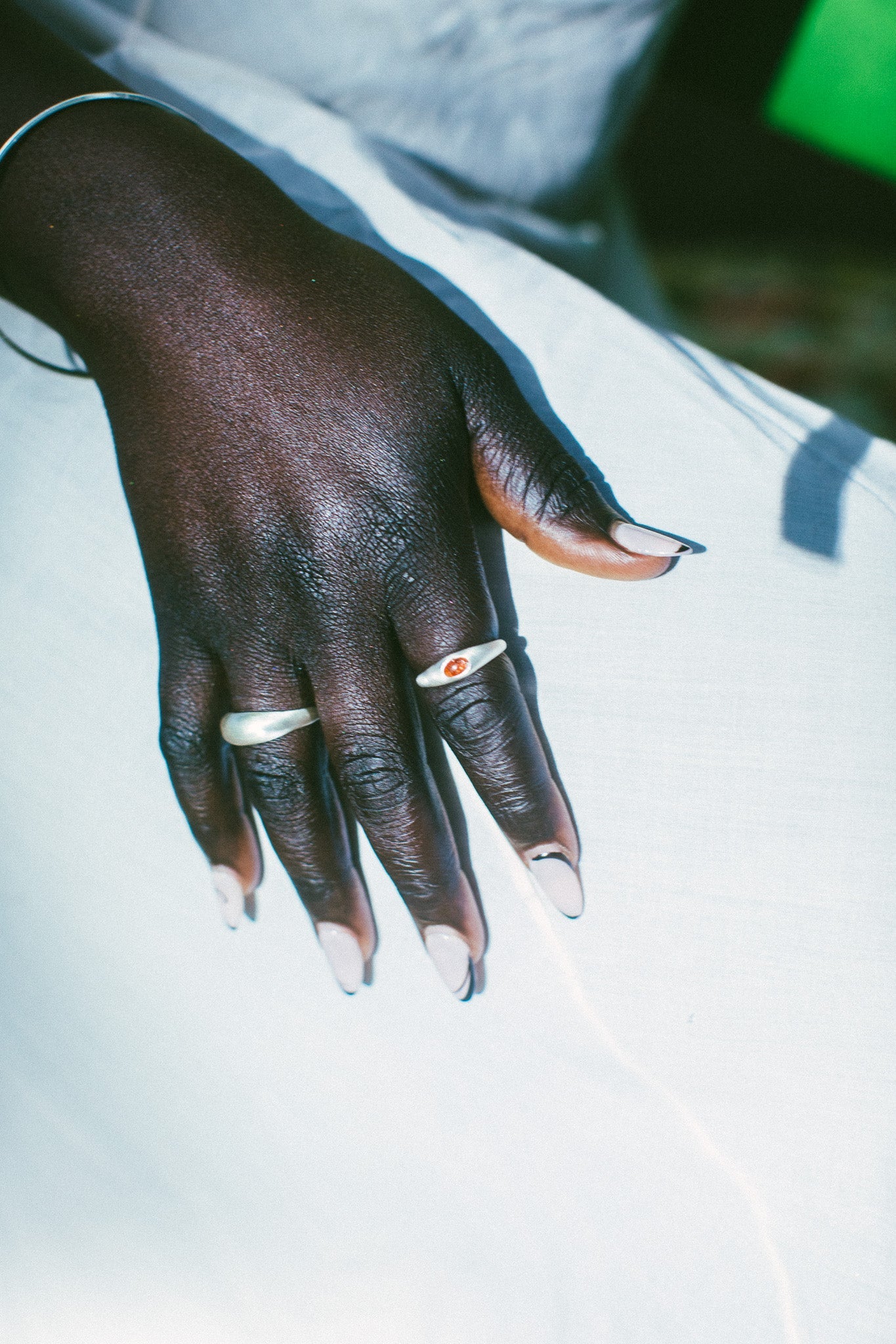 A close-up of a hand wearing two silver rings, resting on a white surface.