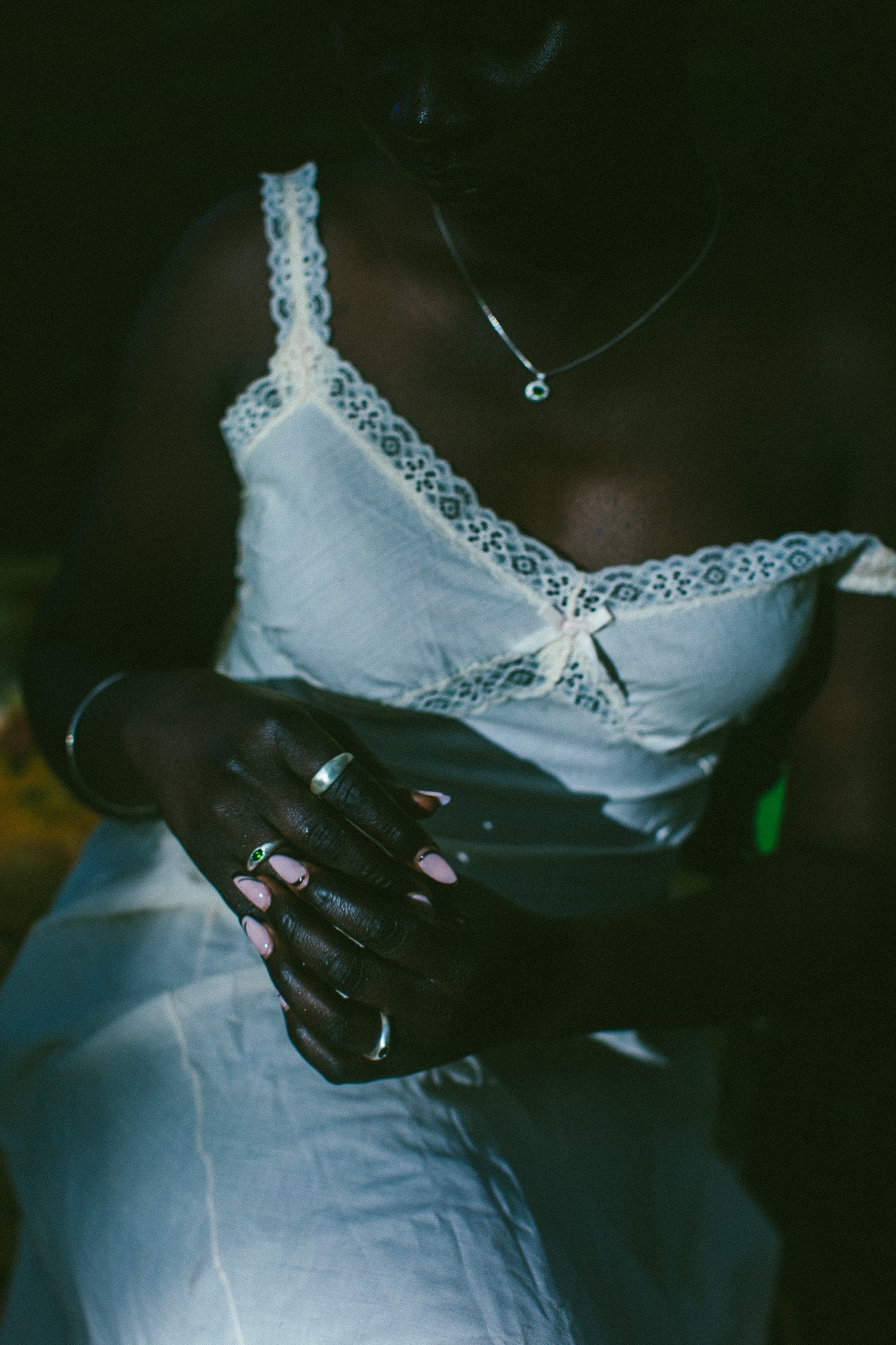 A close-up lifestyle shot of a person wearing a white lace-trimmed camisole top and white pants, adorned with silver rings.