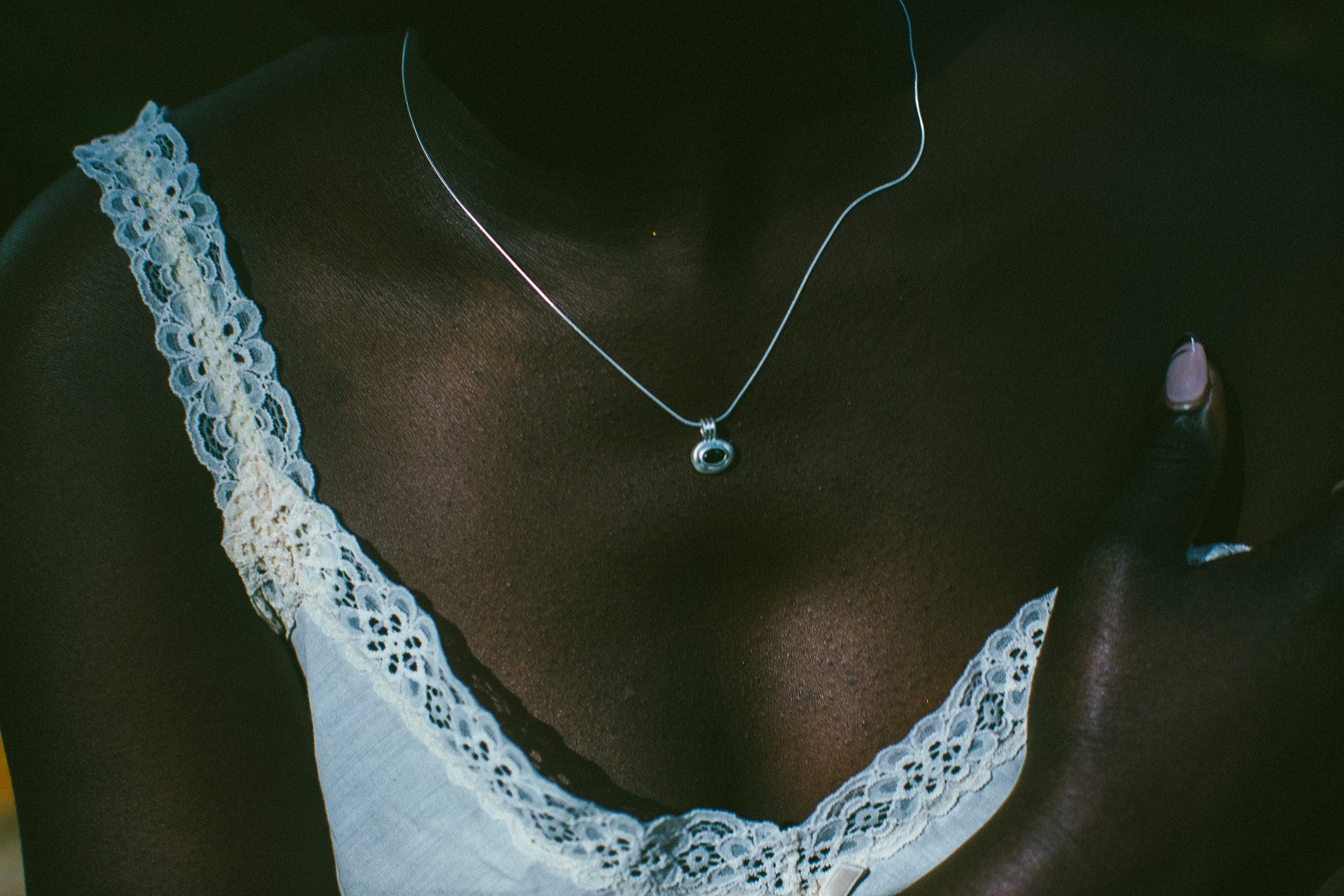 A close-up lifestyle shot of a person wearing a delicate silver chain necklace with a small round pendant, styled with a white lace-trimmed top.