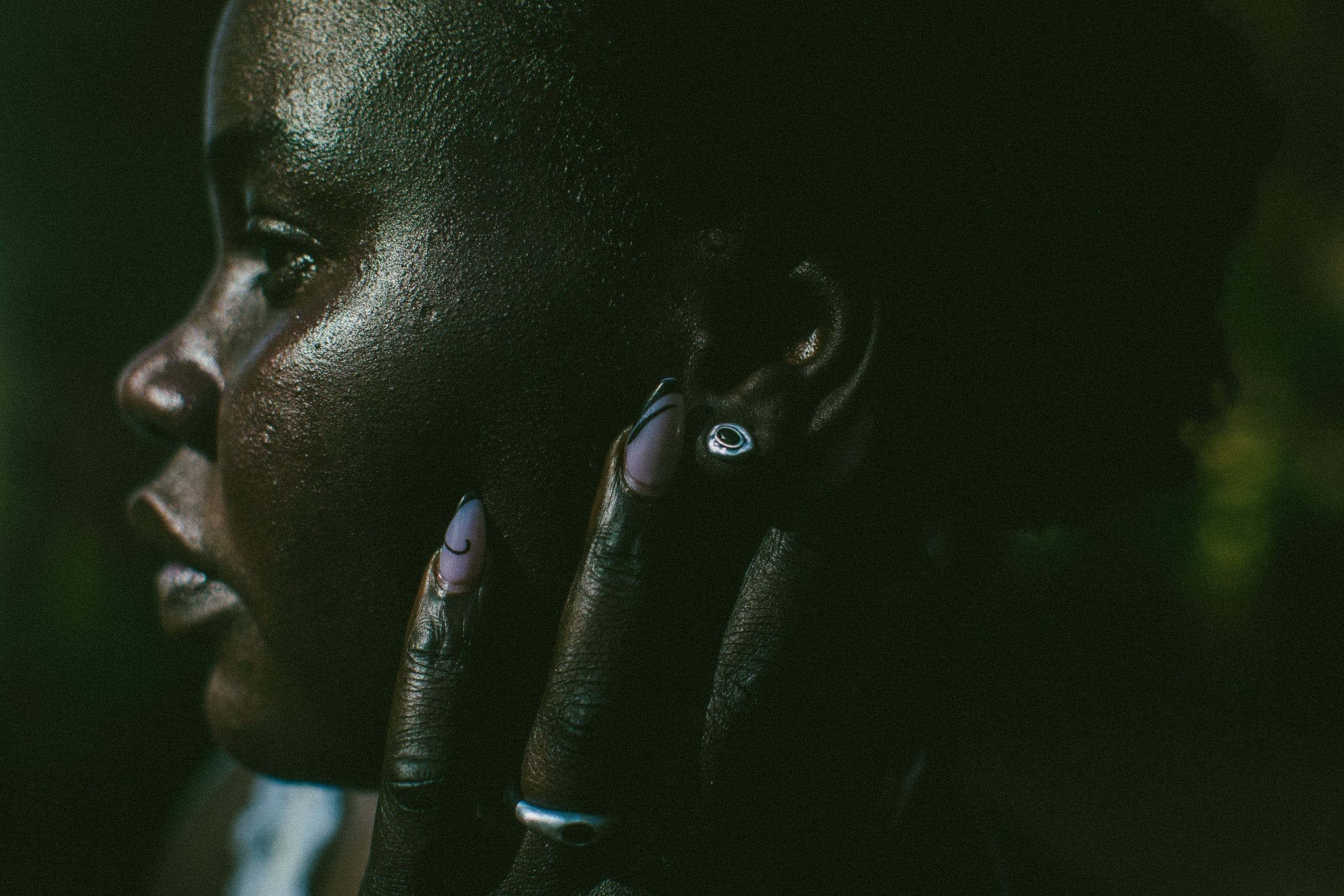 Close-up side profile of a person touching their face, wearing a small silver earring and a silver ring.
