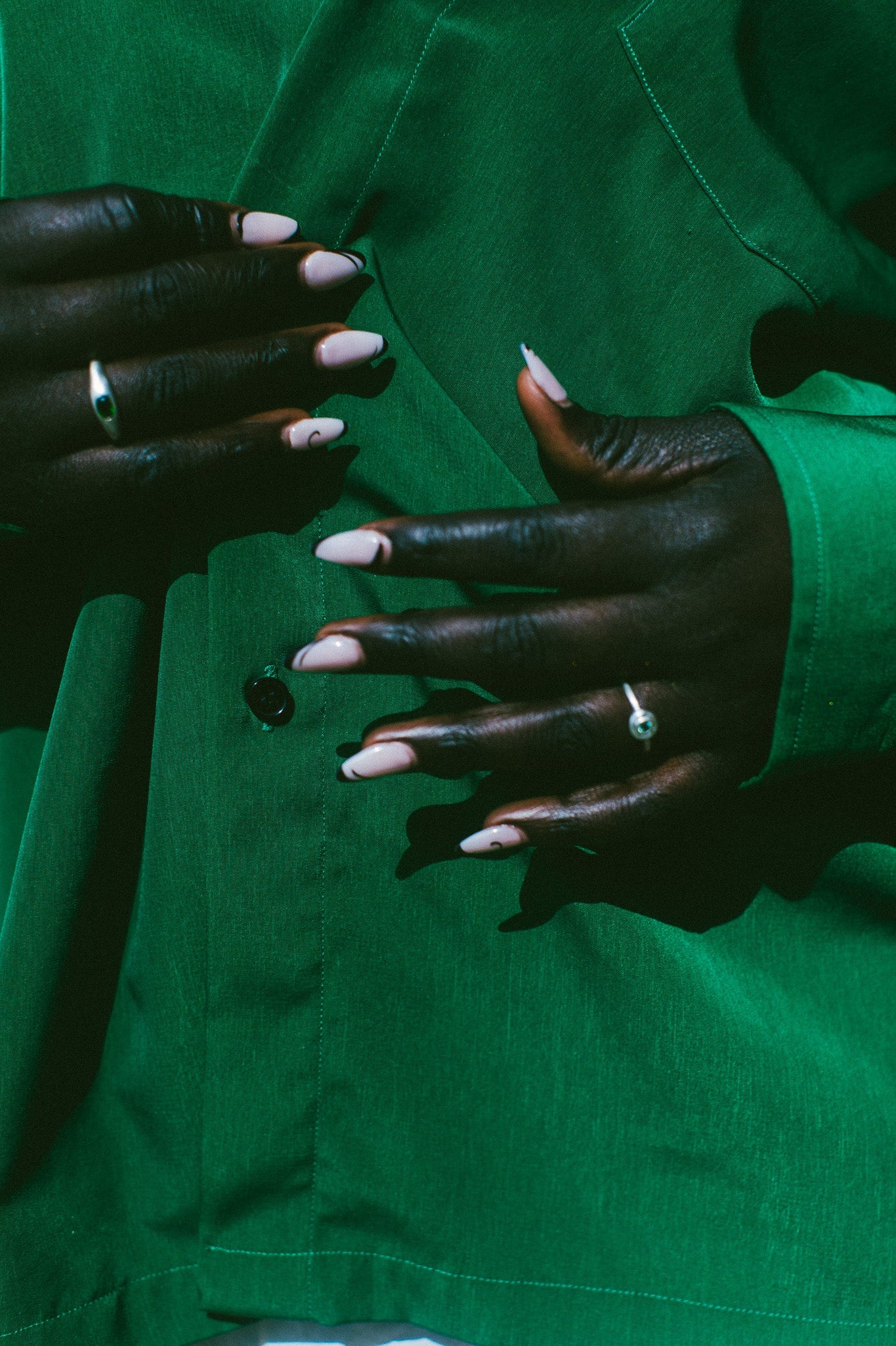 Close-up of a person wearing a bright green button-up shirt, showing both hands with pale pink manicured nails and rings.