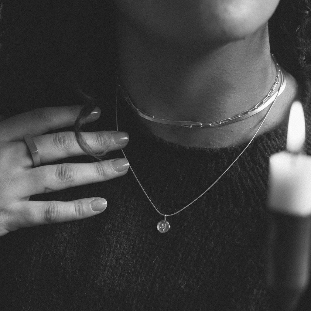 black and white photo of woman wearing two ilver chain necklaces and a silver zodiac pendant necklace