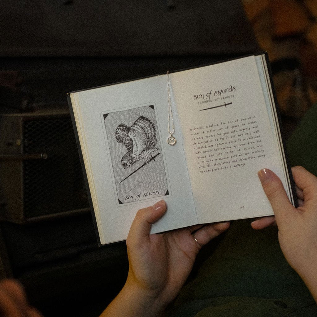 close up of hands holding a tarot book with a zodiac necklace hanging in the middle 
