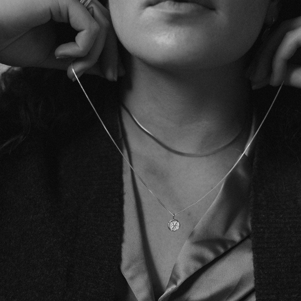 Black and white photo of woman putting on a silver zodiac pendant necklace.