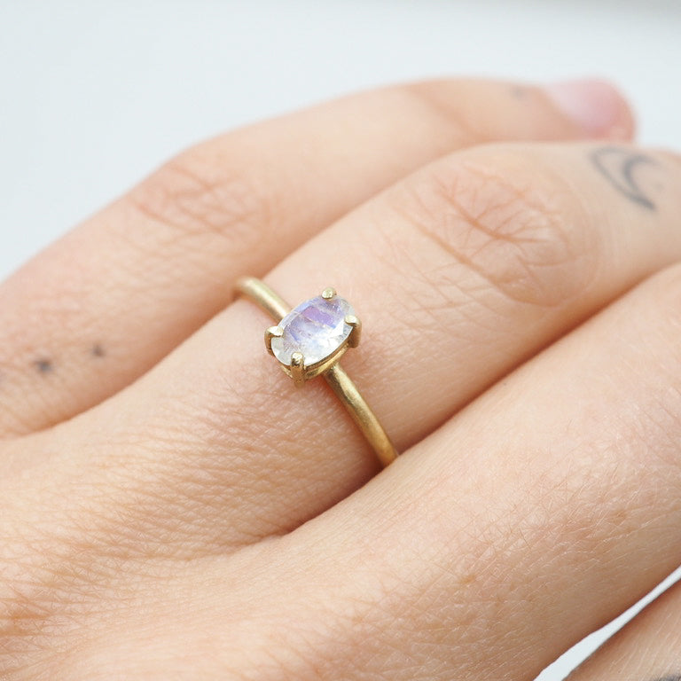 Gold ring with a white gemstone on a hand against a light background