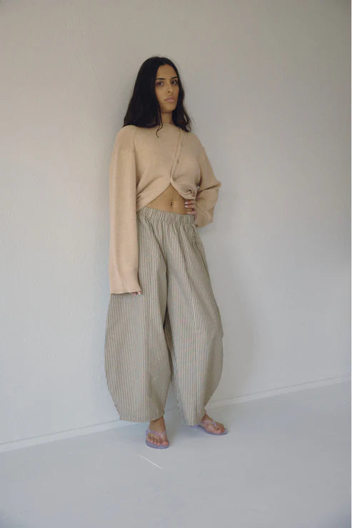 Woman wearing a beige top and striped pants against a plain white background