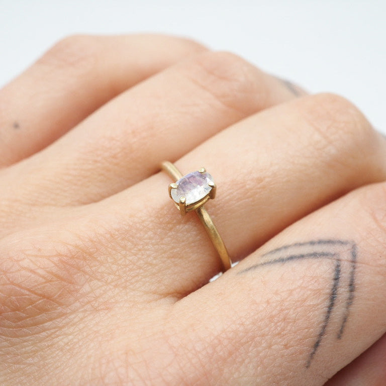 Gold ring with a white gemstone on a person's finger against a white background