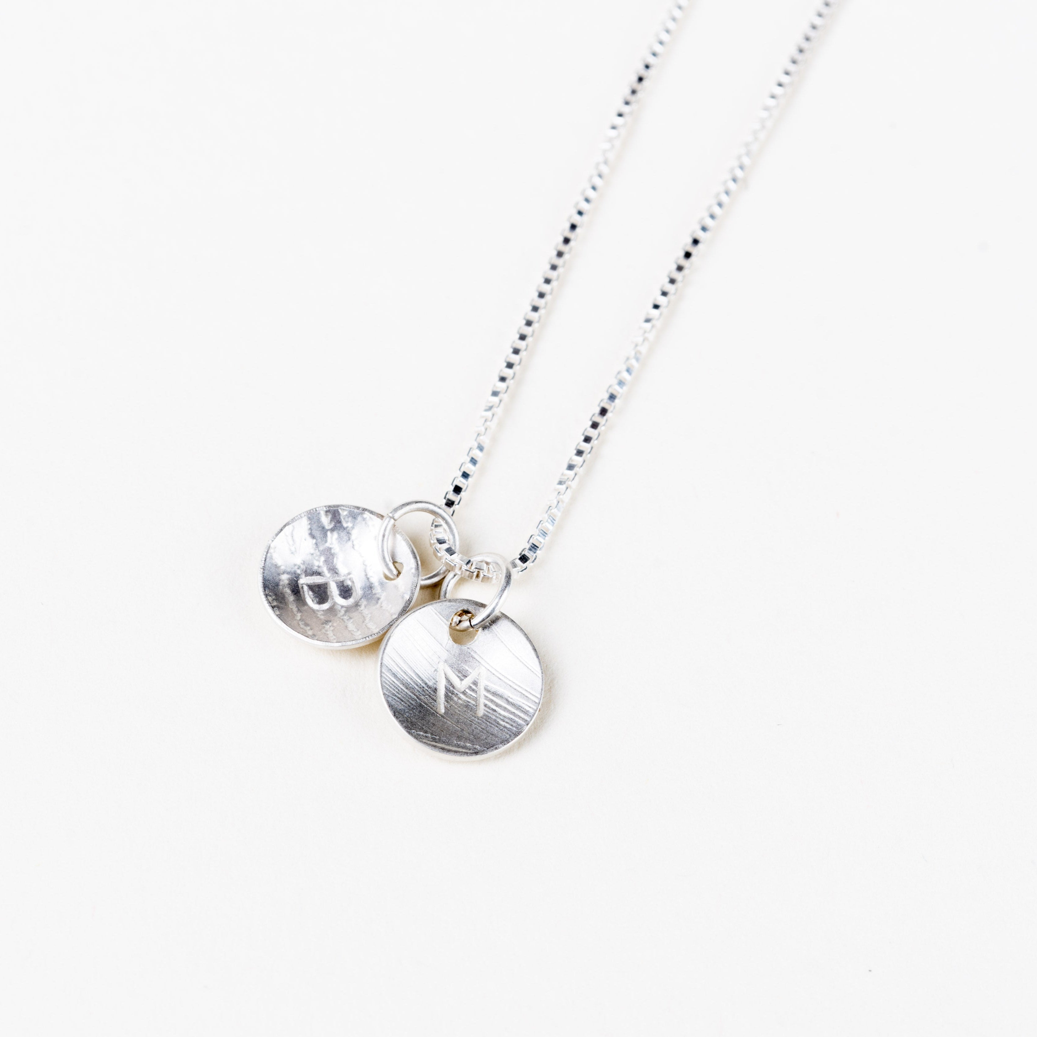 Silver necklace with two round pendants with letters on a white background