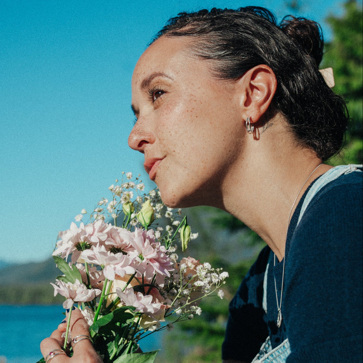 Woman holding a bouquet of flowers by a body of water with mountains in the background