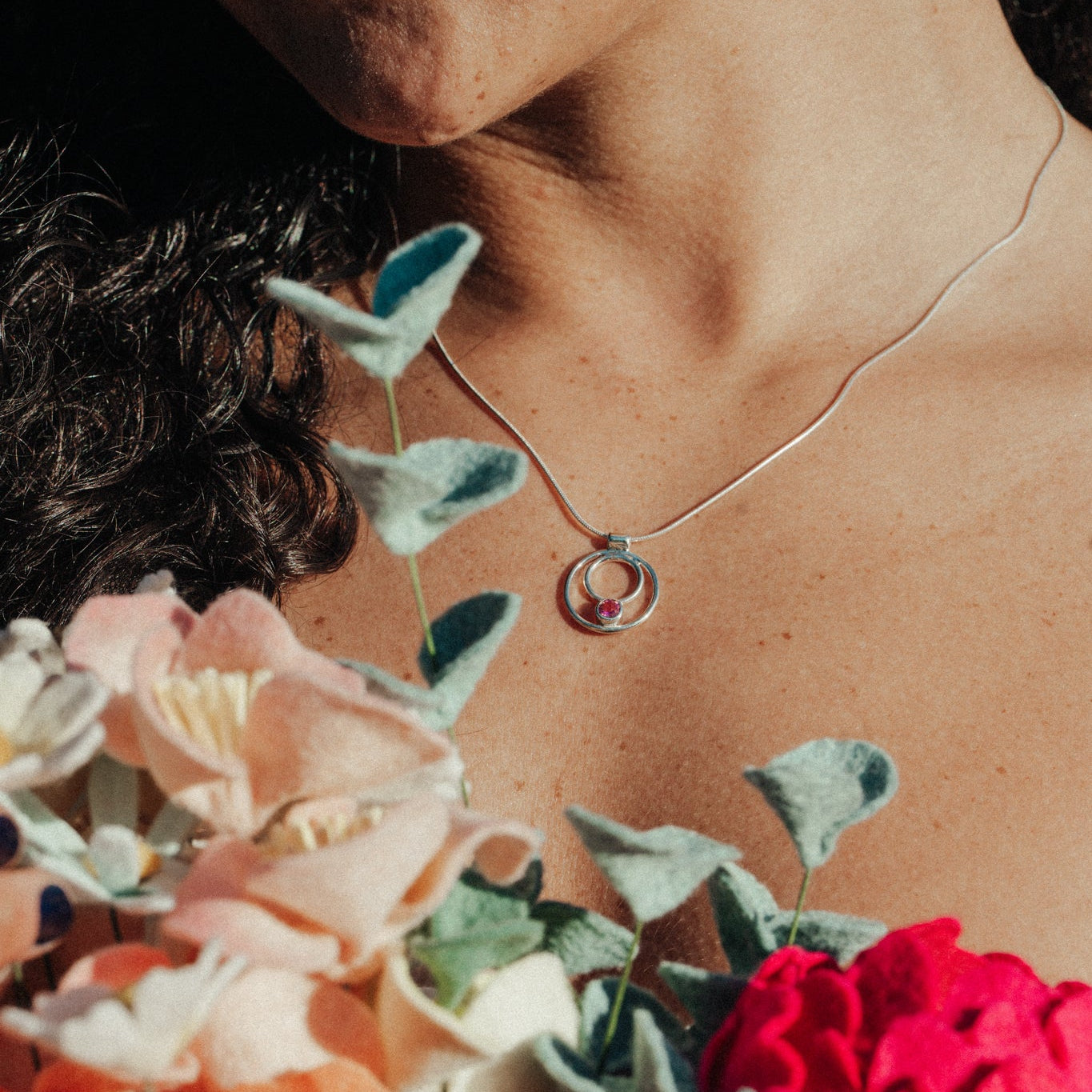 Person holding flowers with a necklace featuring a circular pendant.