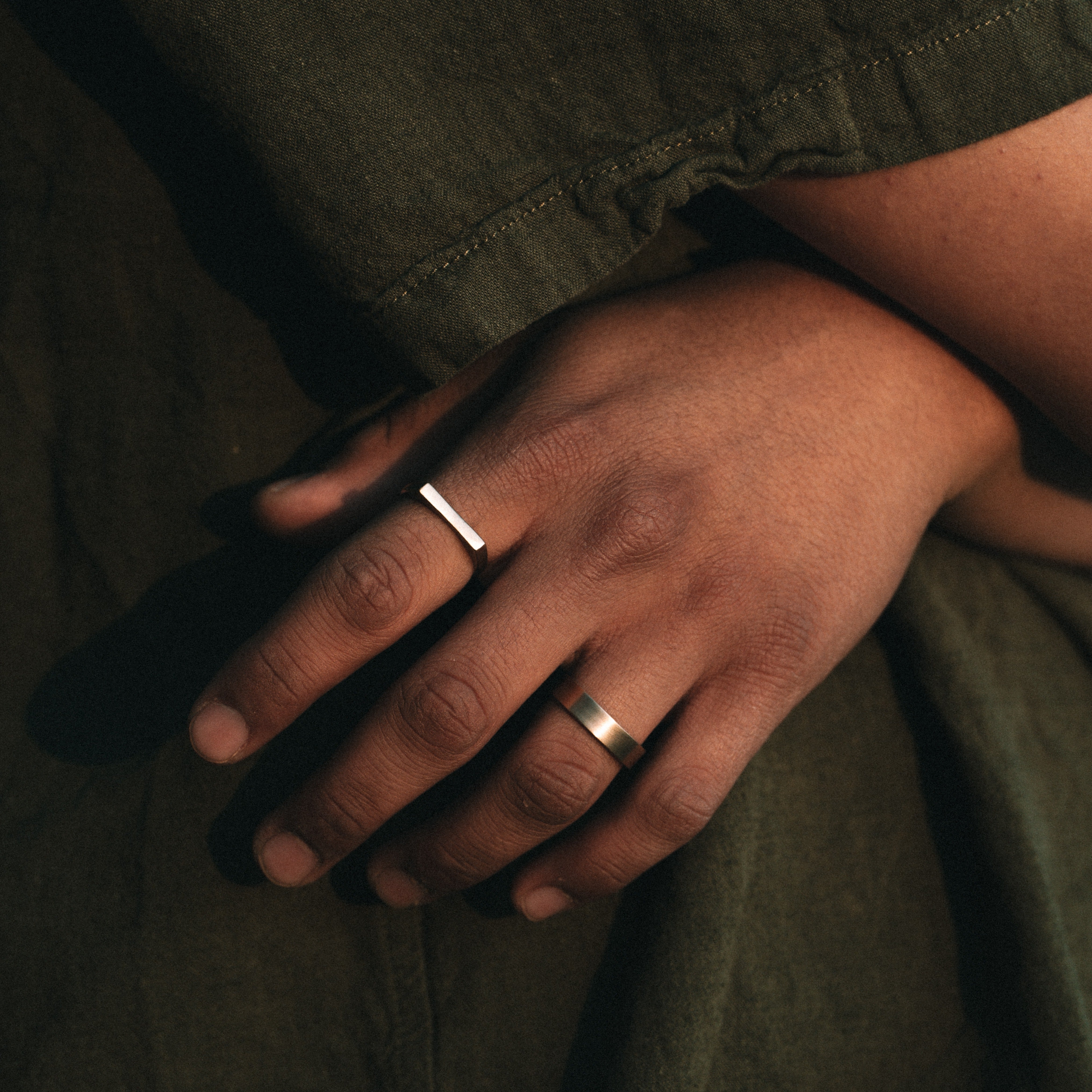 Close-up of a hand wearing two rings on a dark background