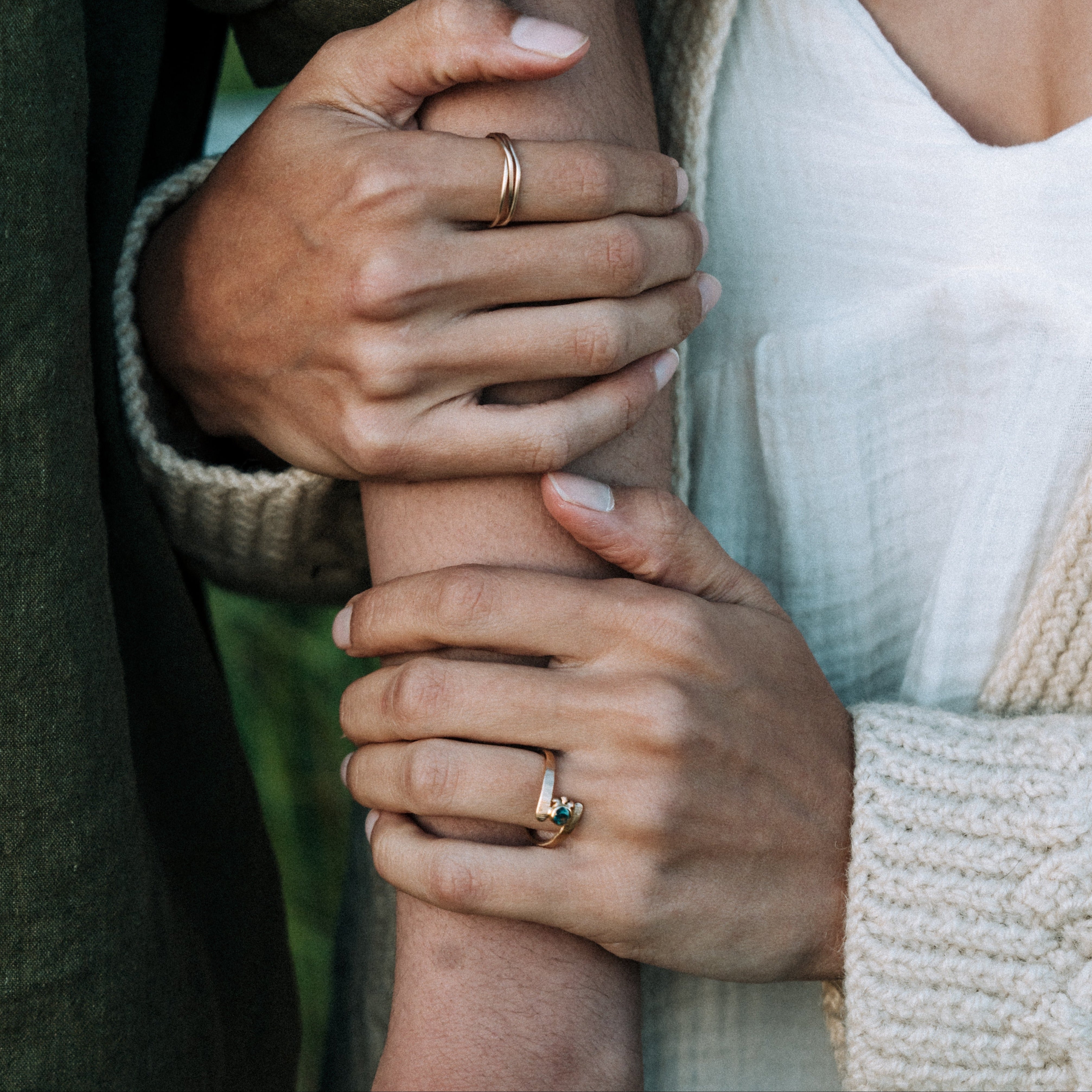 Close-up of two hands holding each other with visible rings, wearing green and beige clothing.