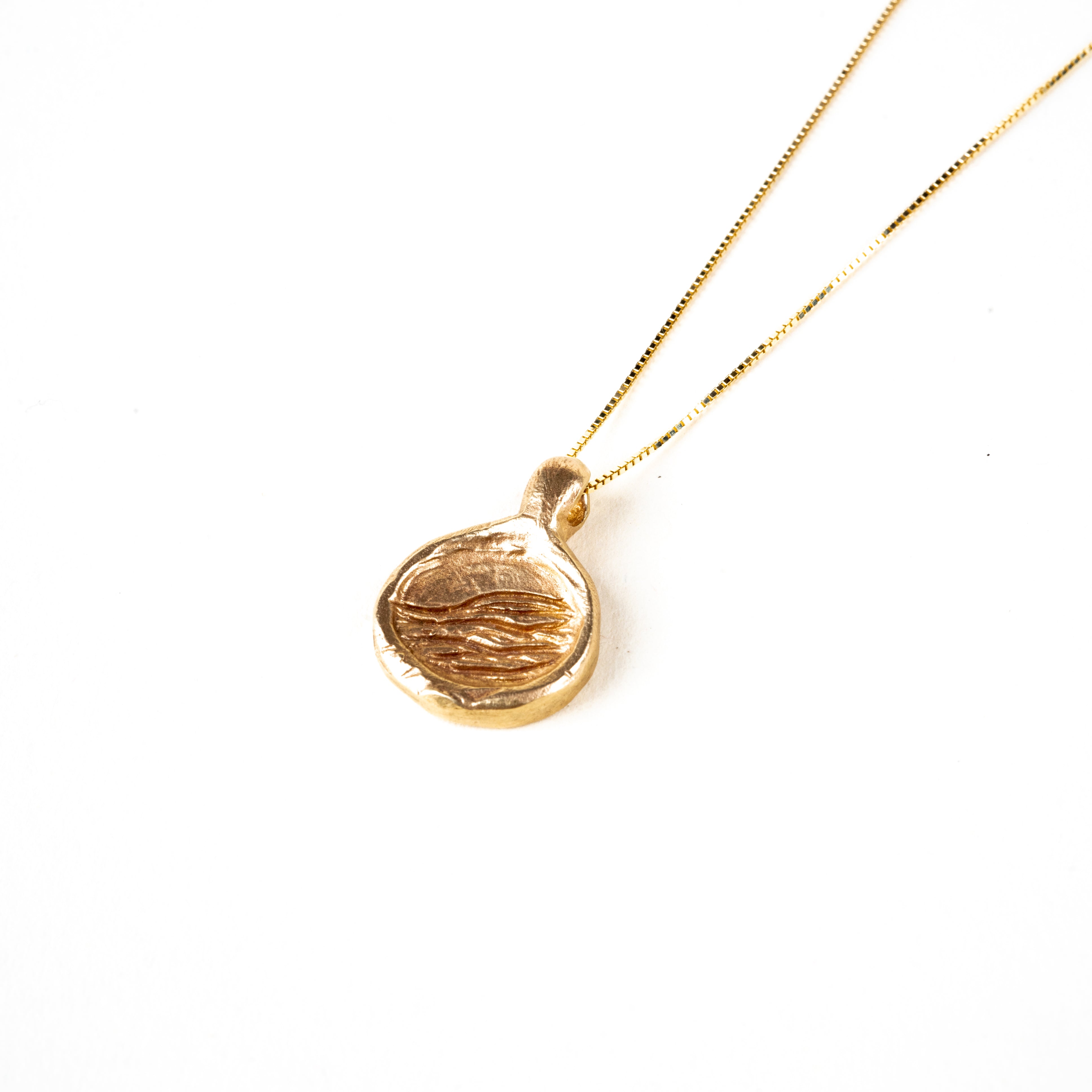 A 10K gold necklace with a carved pendant on a gold chain, displayed against a white background.