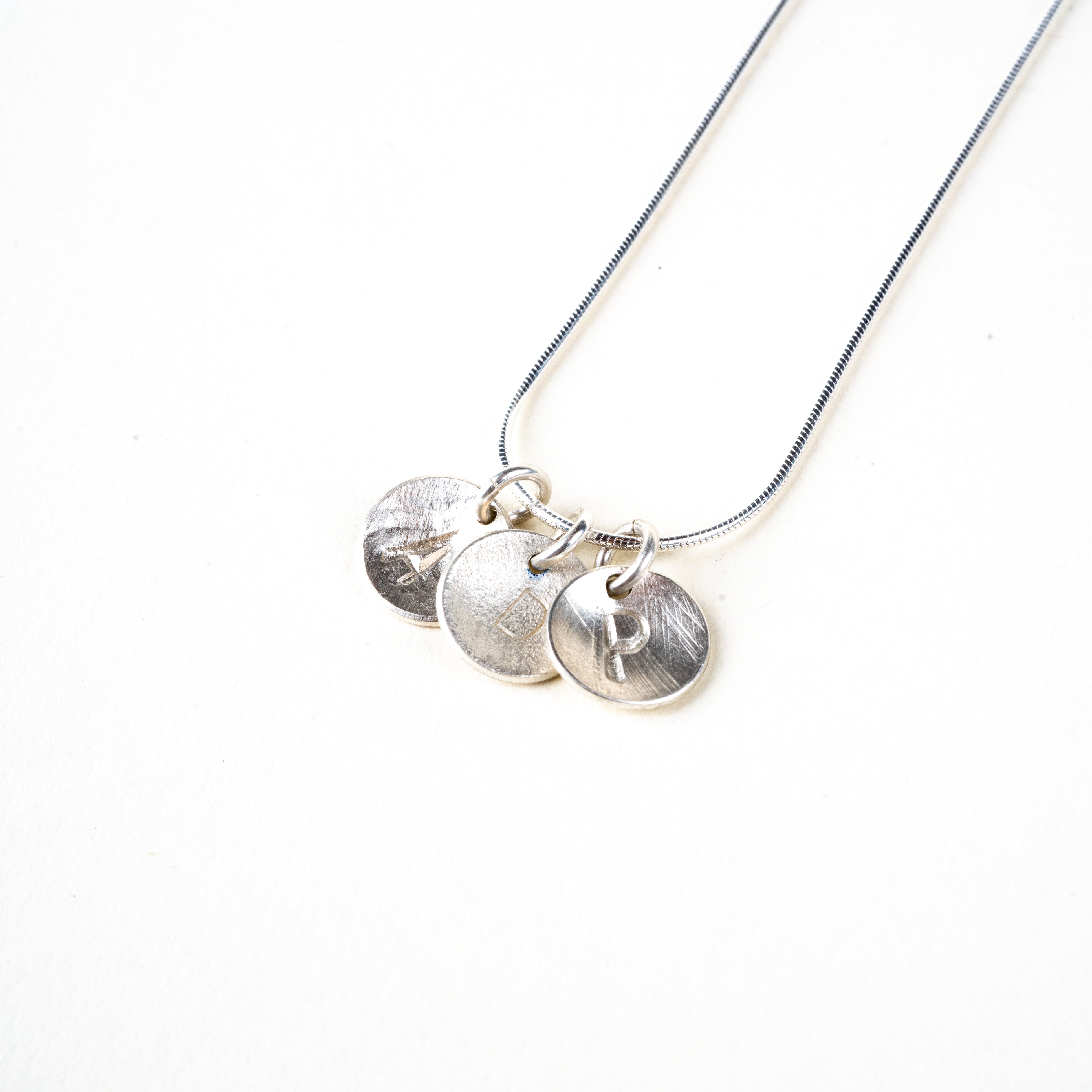 Silver necklace with 3 round pendants with letters on a white background