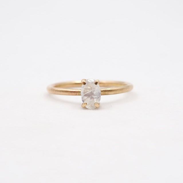 Gold ring with a white gemstone on a light beige background
