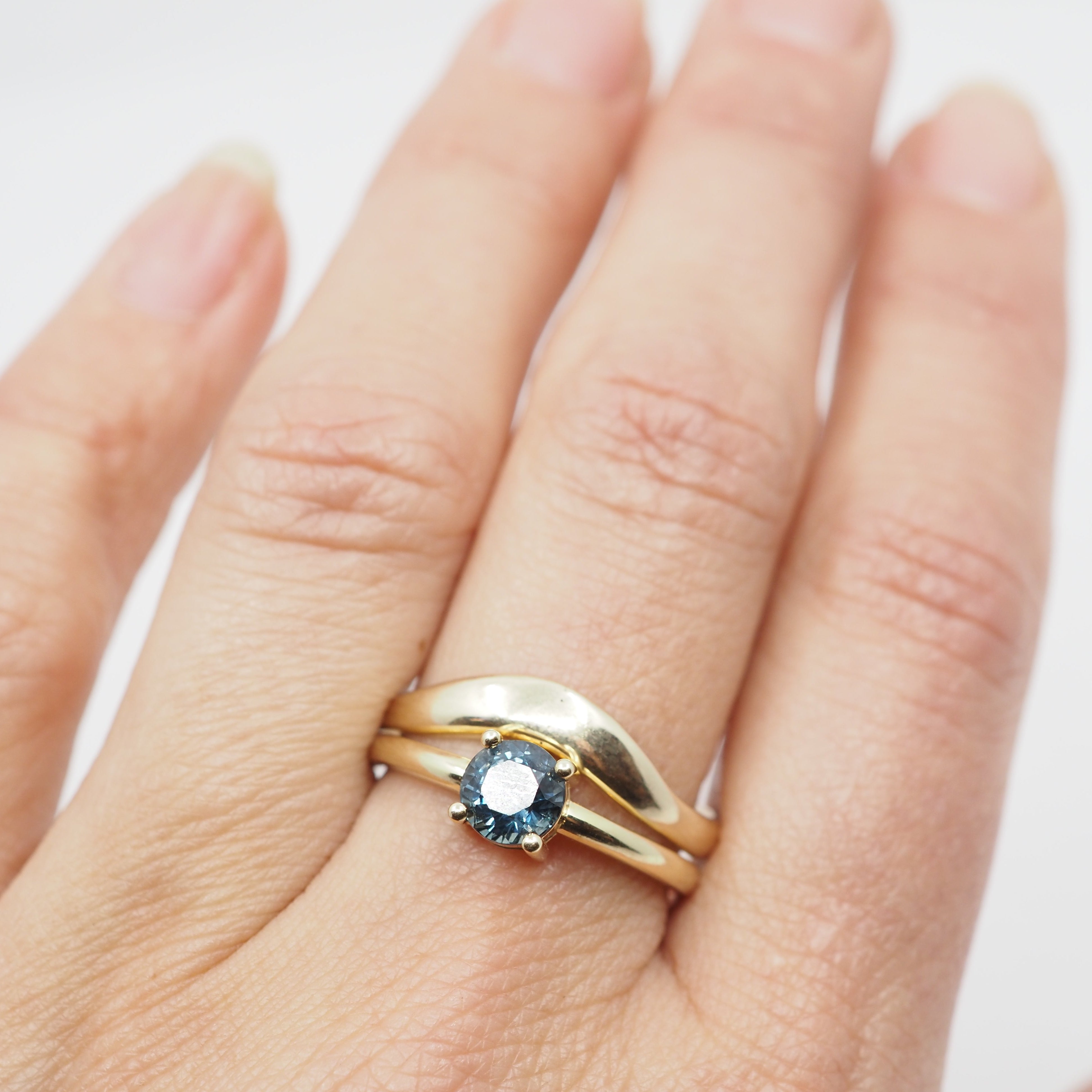 Gold ring stacked with a gold ring with a blue gemstone on a hand against a white background