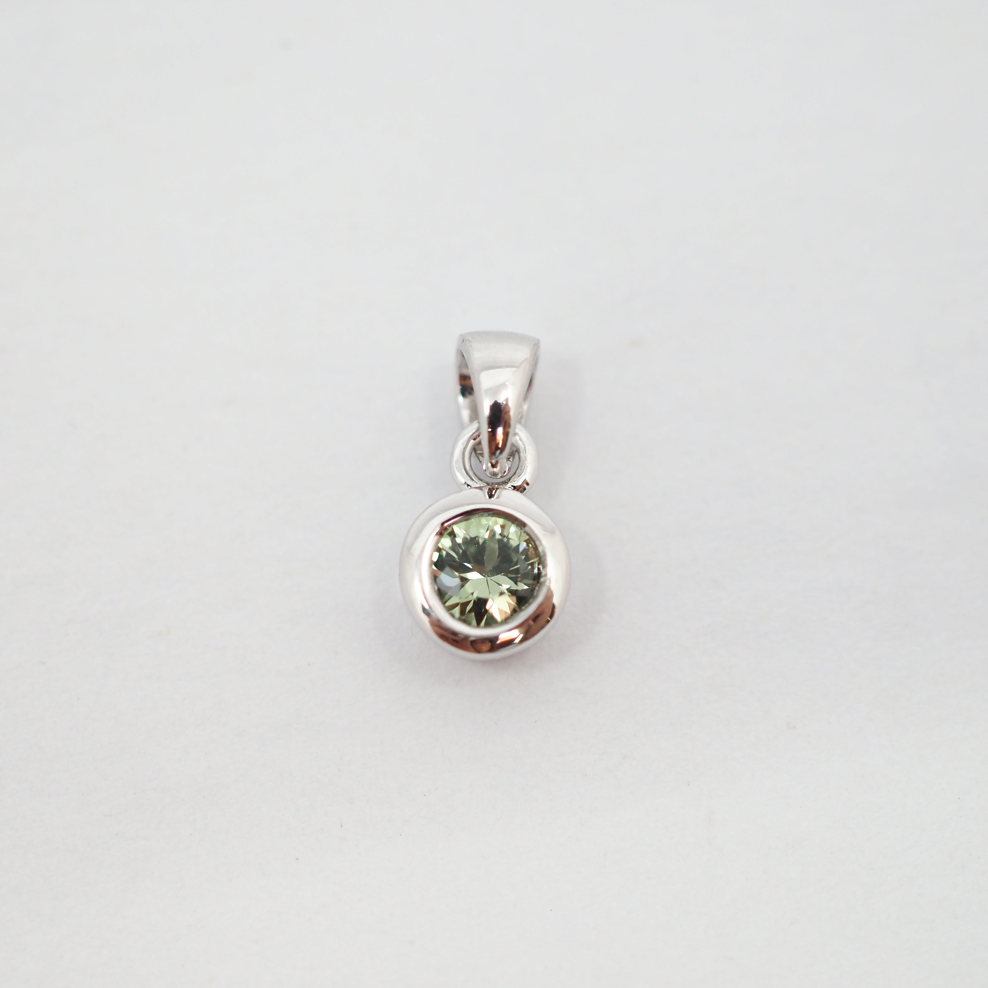 A sterling silver pendant featuring a bezel-set round light green gemstone, shown against a plain light gray background.