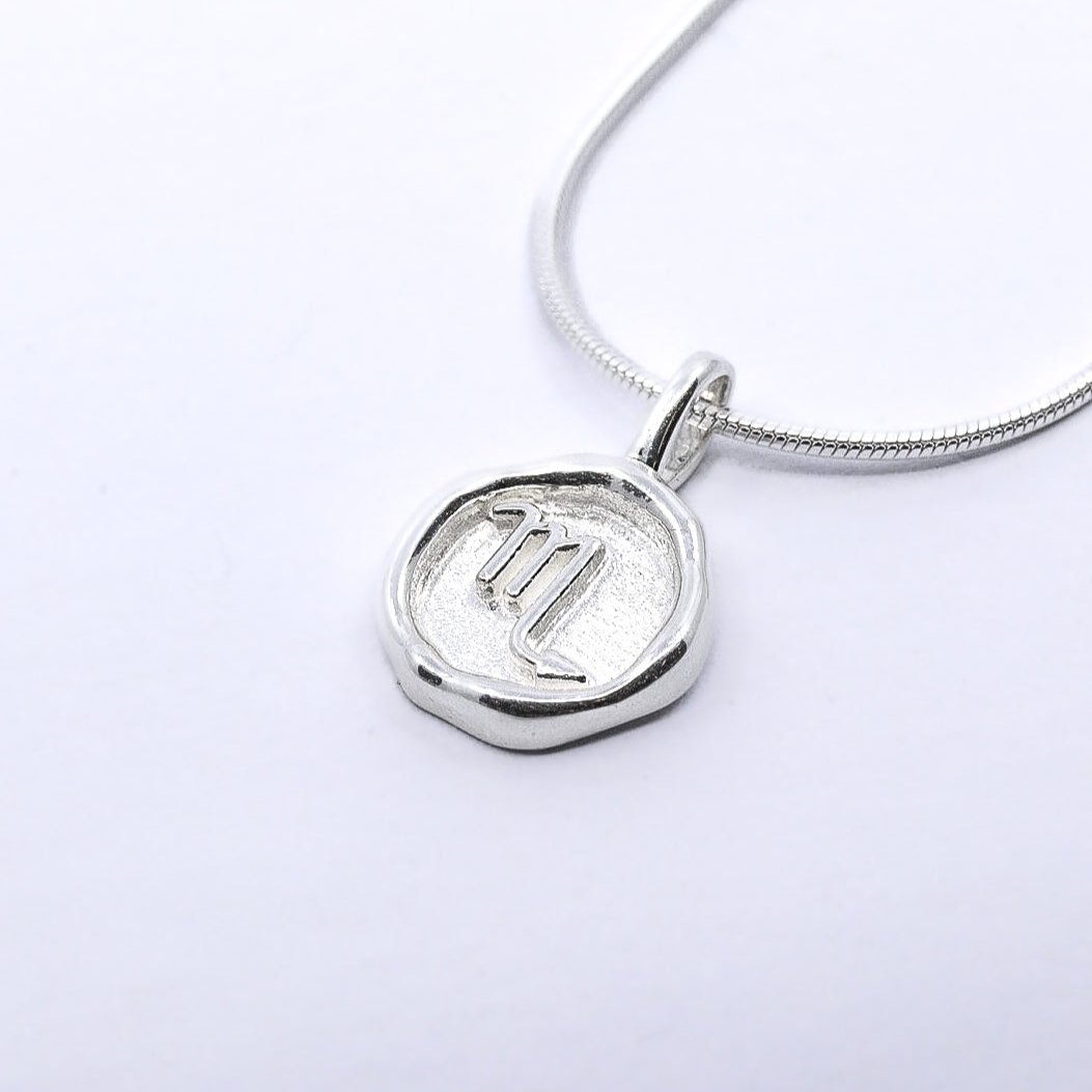 A silver necklace featuring a round pendant with a zodiac sign on it, attached to a delicate chain.