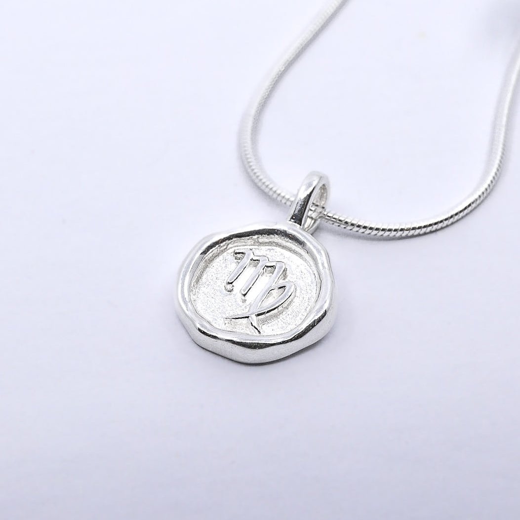 A silver necklace featuring a round pendant with a zodiac sign on it, attached to a delicate chain.