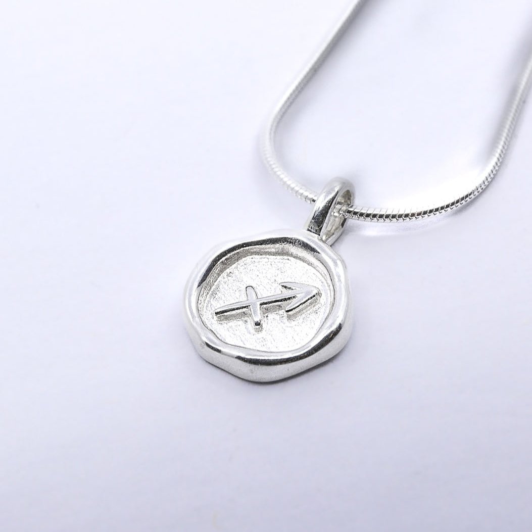 A silver necklace featuring a round pendant with a zodiac sign symbol on it, attached to a chain.