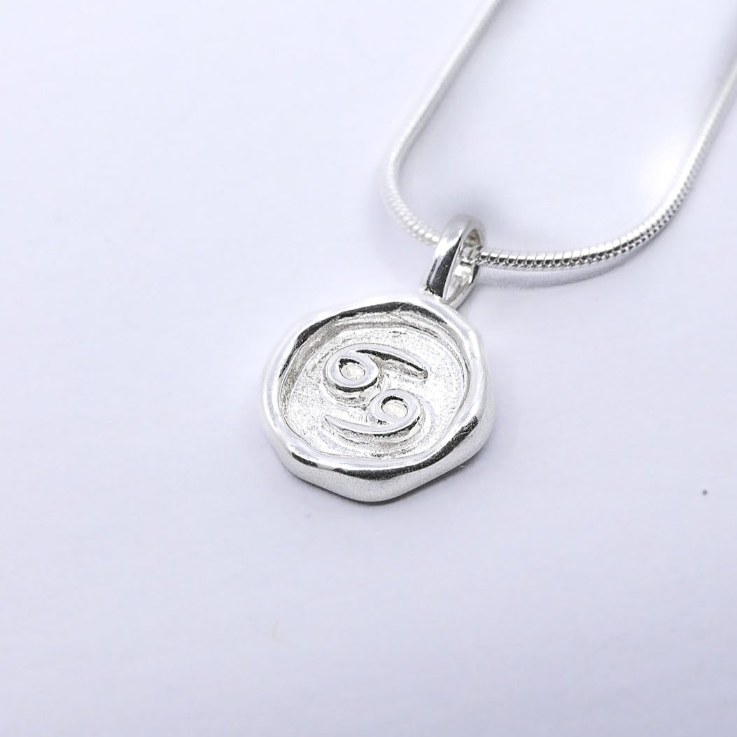 A silver pendant necklace with a round pendant featuring a star sign, attached to a chain.