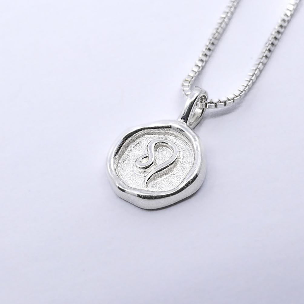 A silver necklace featuring a round pendant with a zodiac sign on it, attached to a delicate chain.