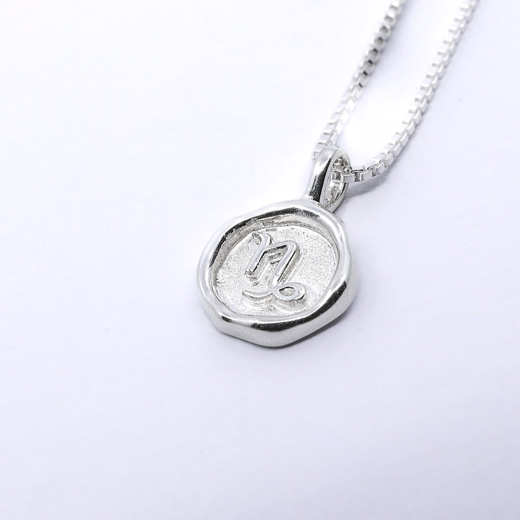 A silver necklace featuring a round pendant with a zodiac sign on it, attached to a delicate chain.
