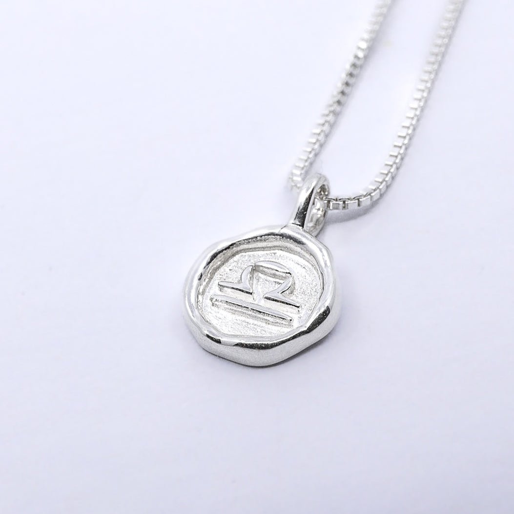 A silver necklace featuring a round pendant with a zodiac sign on it, attached to a delicate chain.