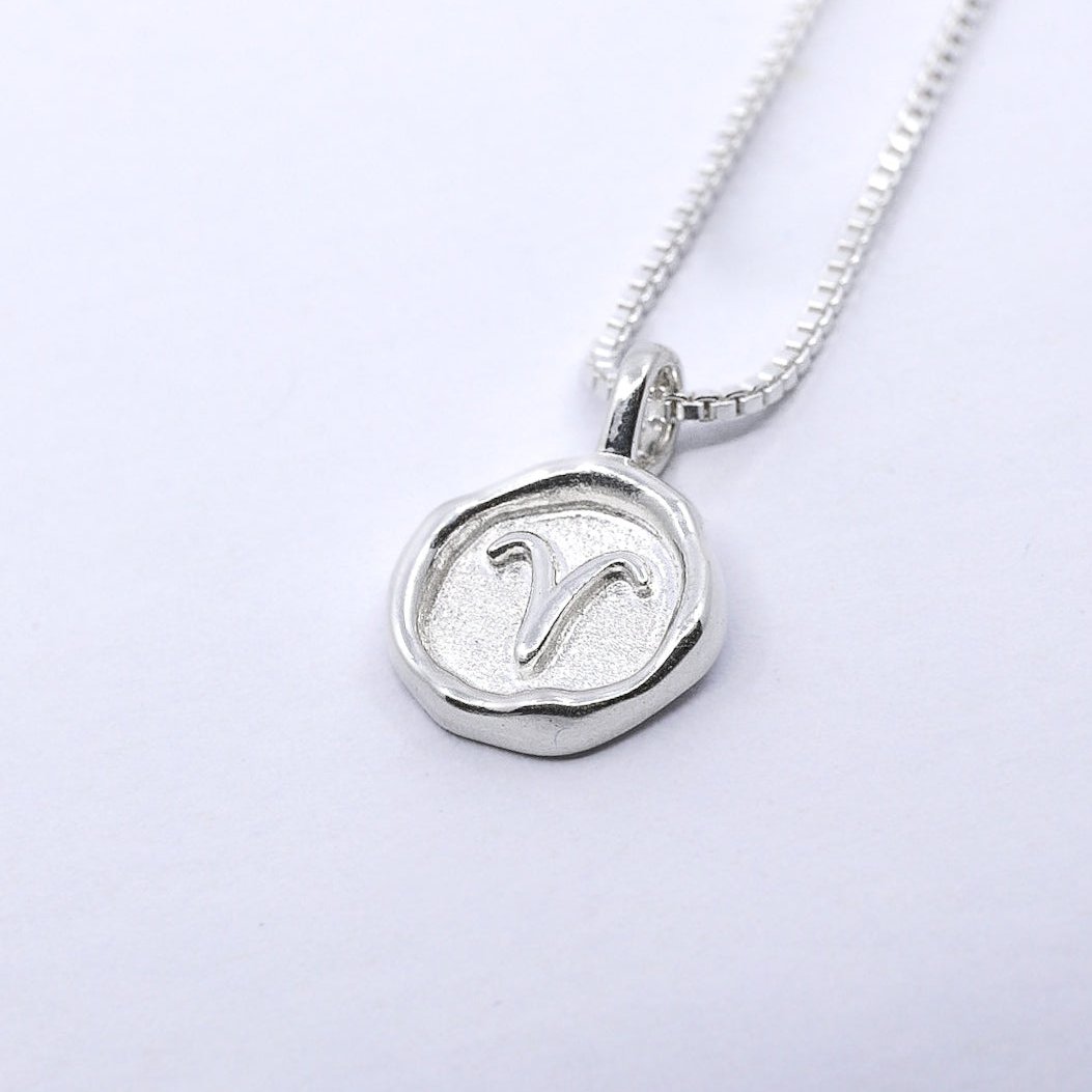 A silver necklace featuring a round pendant with a zodiac sign on it, attached to a delicate chain.