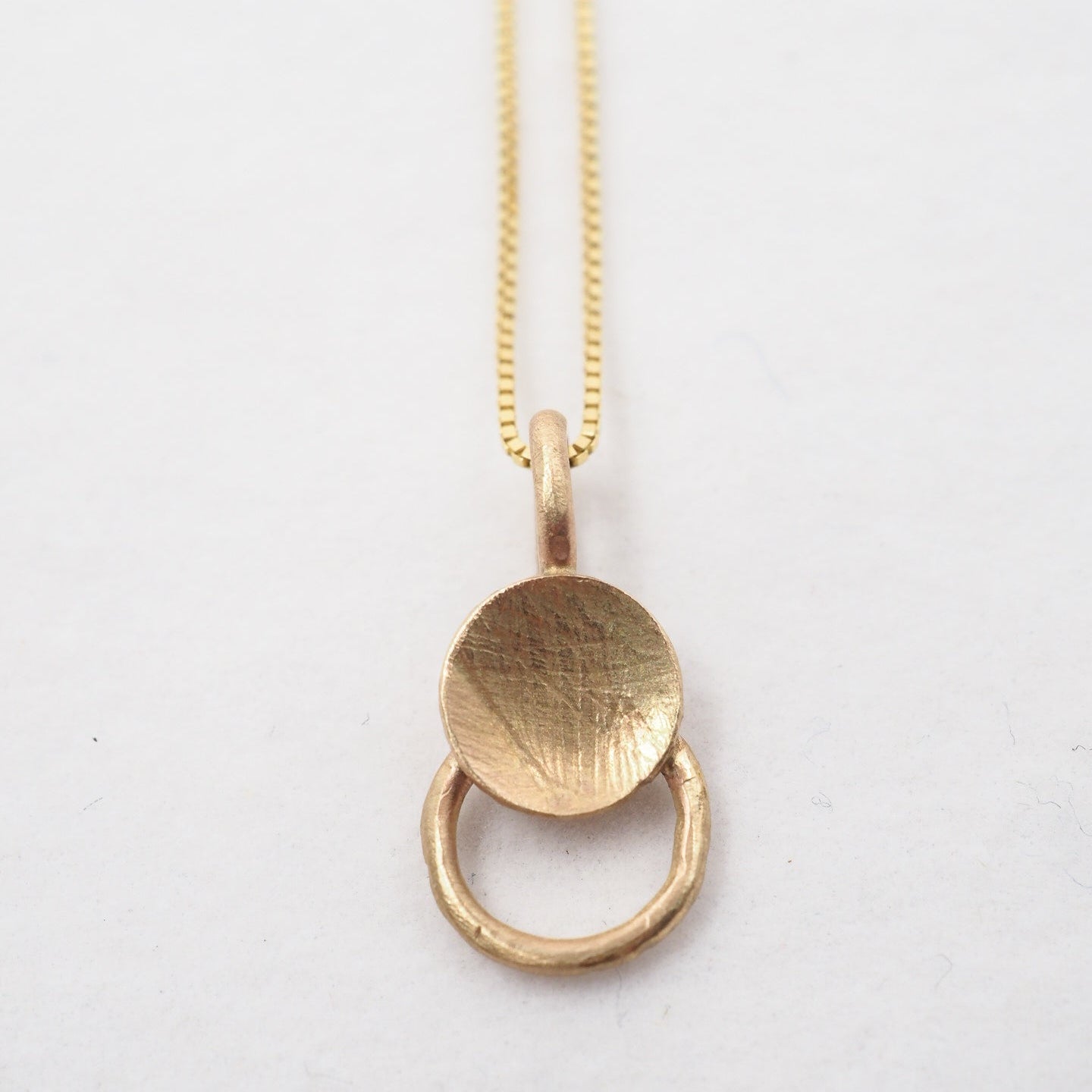 Gold necklace with a circular pendant on a white background