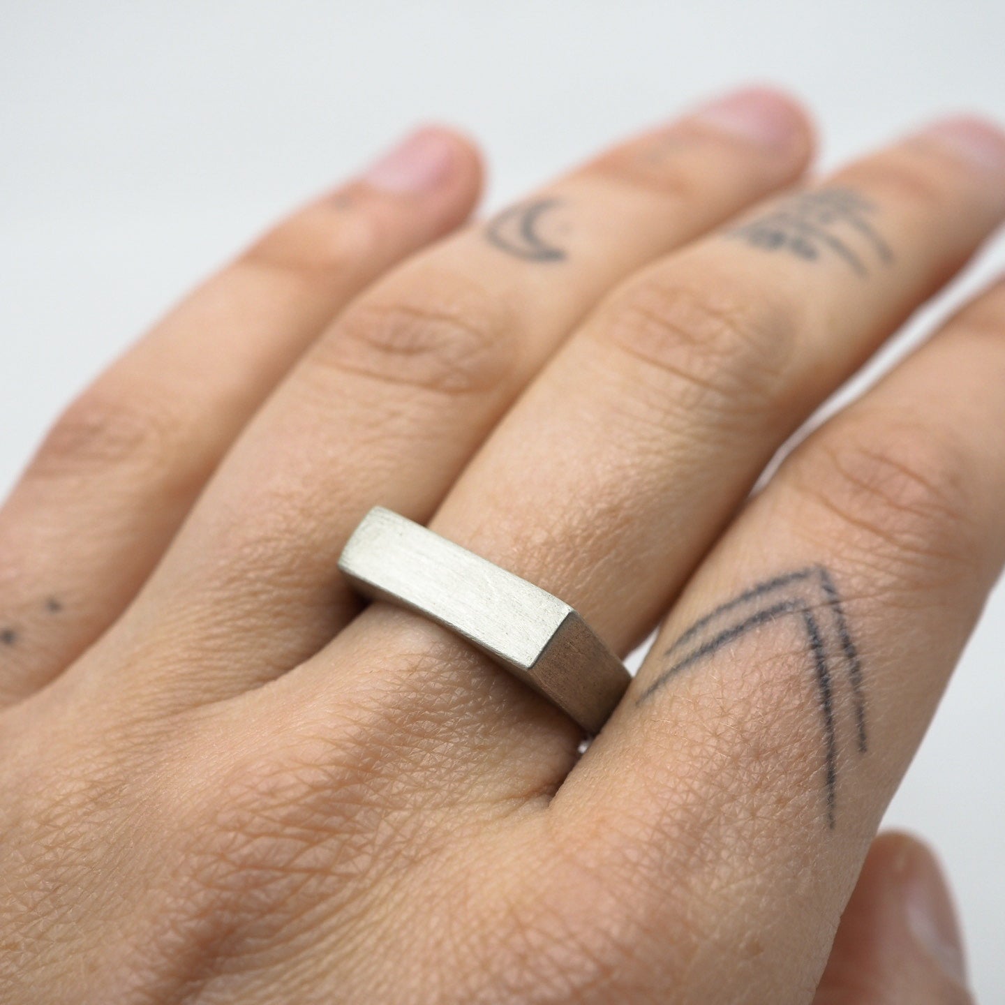 Hand wearing a silver ring on a plain background