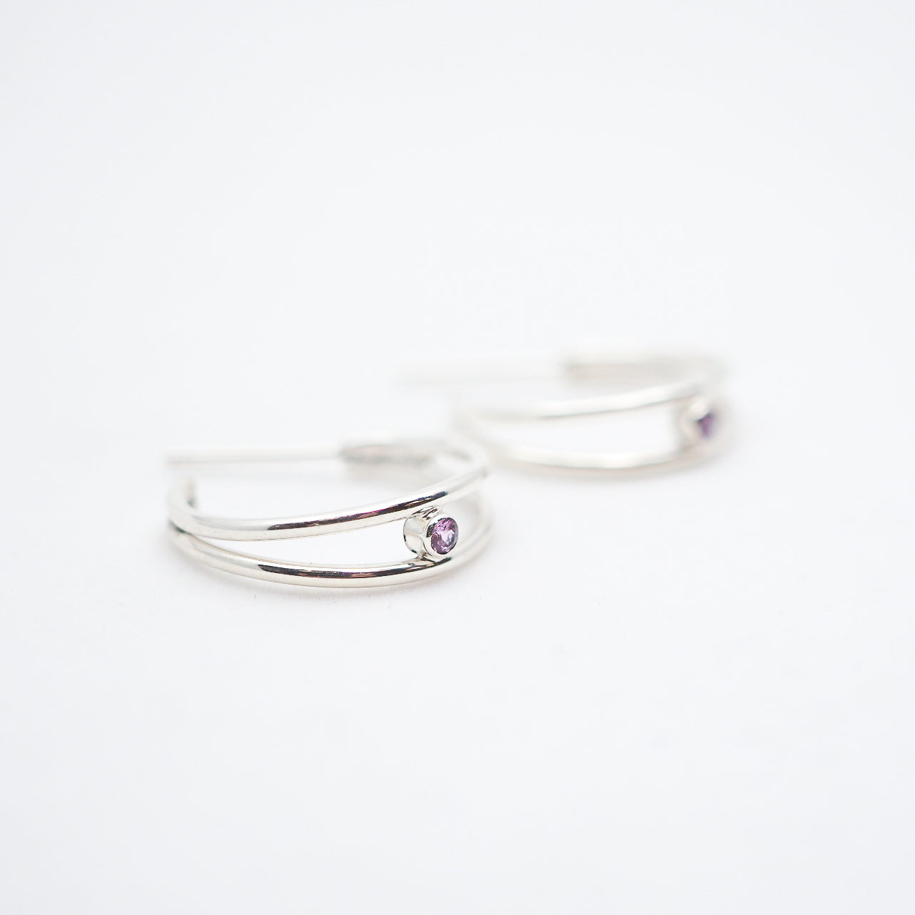 Two silver rings with purple gemstones on a white background