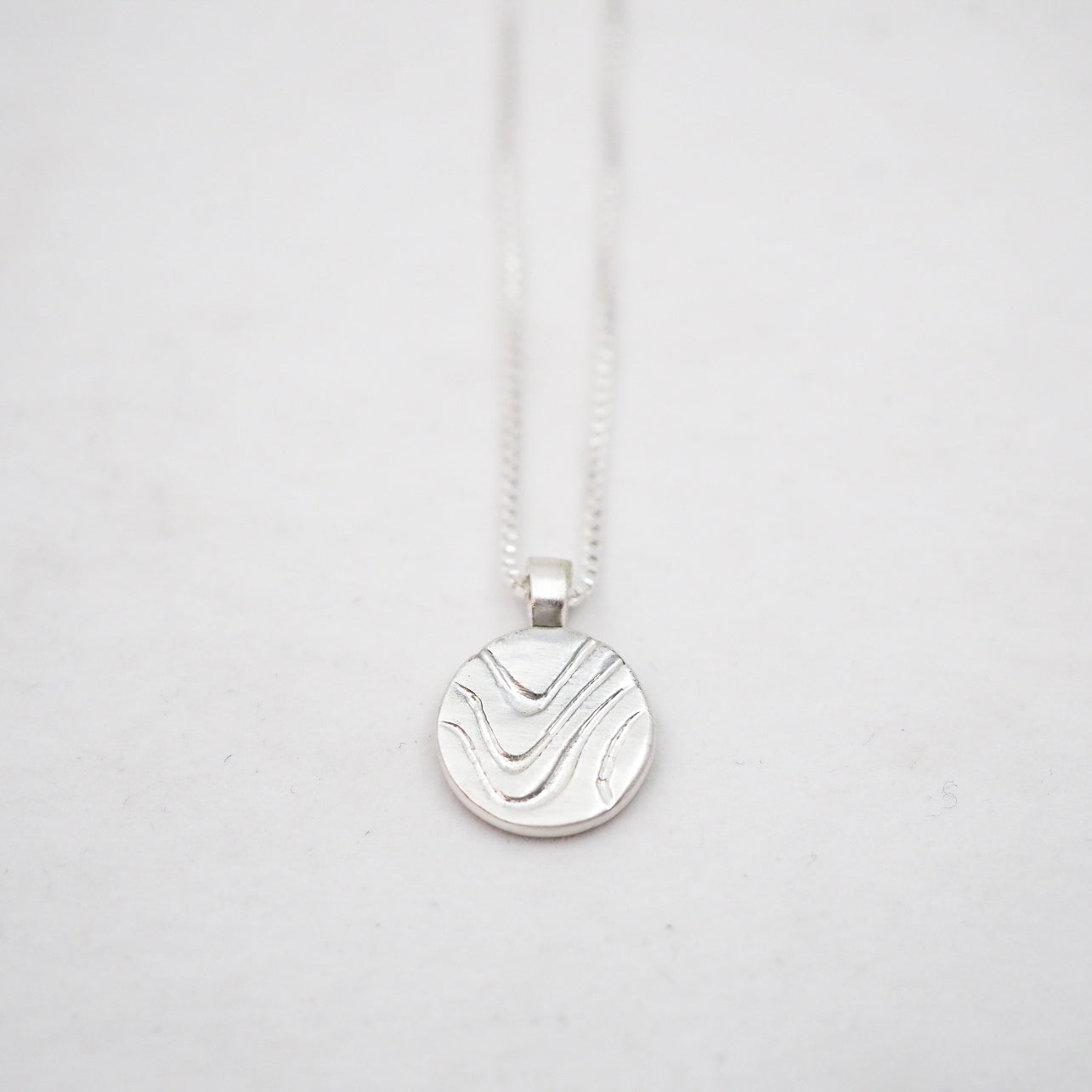 Silver necklace with a round pendant on a light gray background