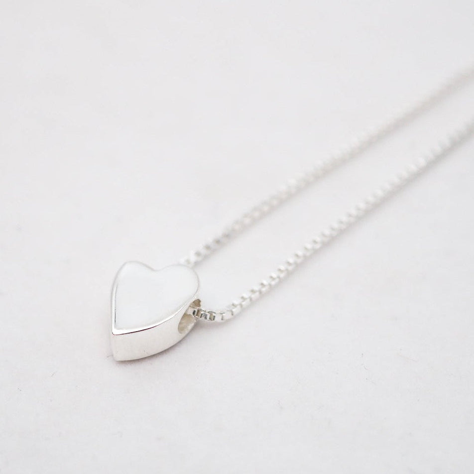 Silver heart-shaped pendant on a chain against a light gray background