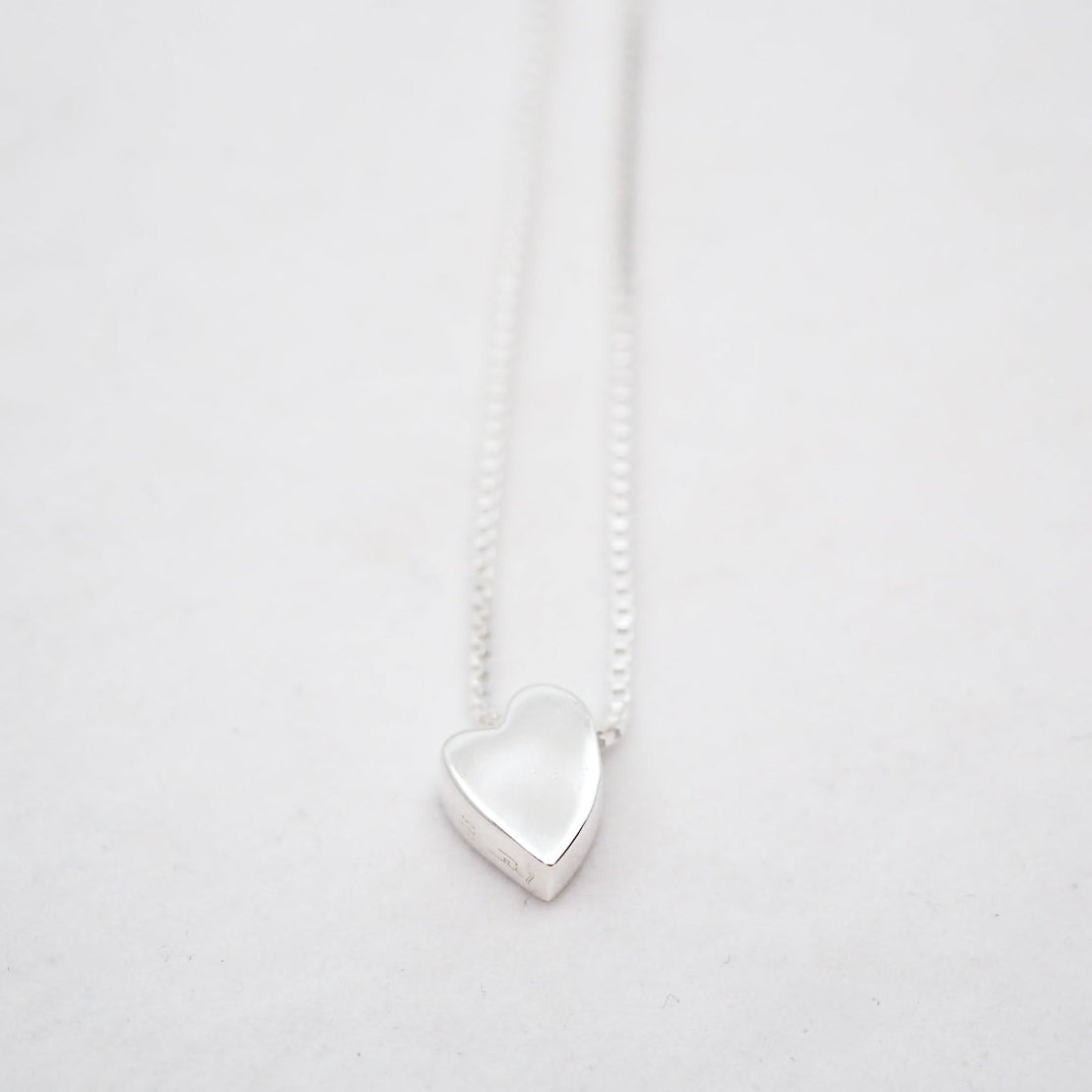 Silver heart-shaped pendant on a white chain against a light gray background