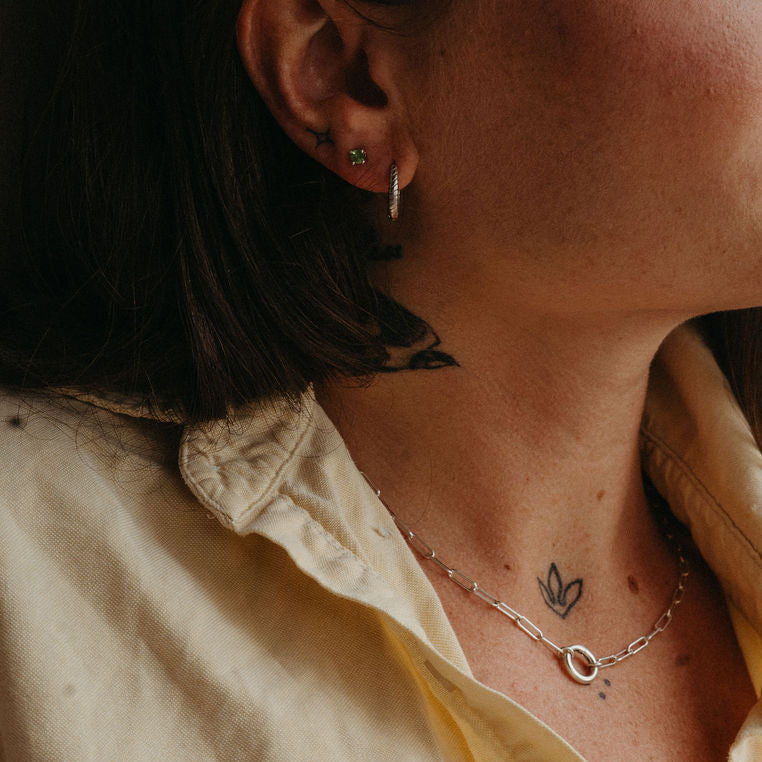 Close-up of a person wearing multiple necklaces and earrings with tattoos on their arm.