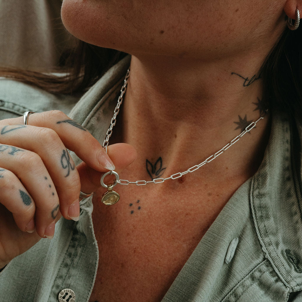 Person wearing a necklace with a small pendant, close-up of neck and tattoos.