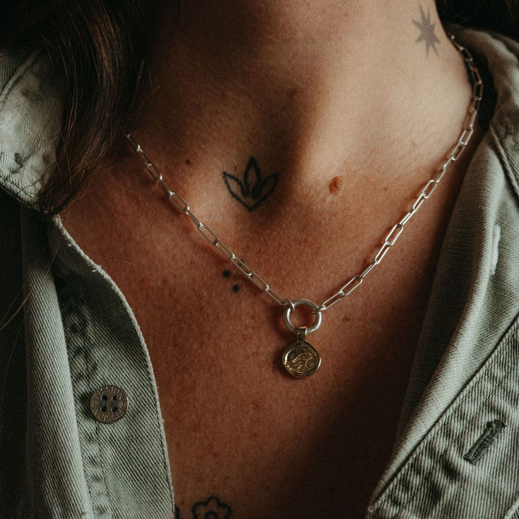 Necklace with a pendant worn by a person, showing tattoos on the neck and shoulders.