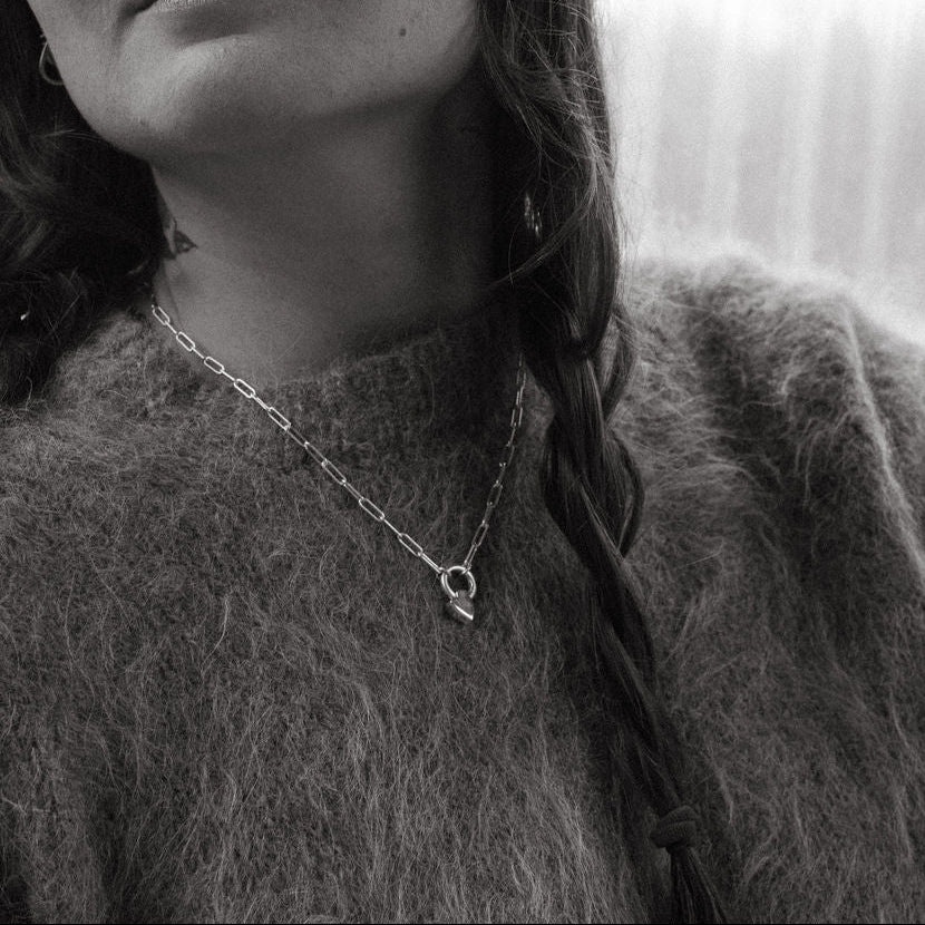 Black and white photo of a person wearing a textured sweater and a heart pendant necklace.