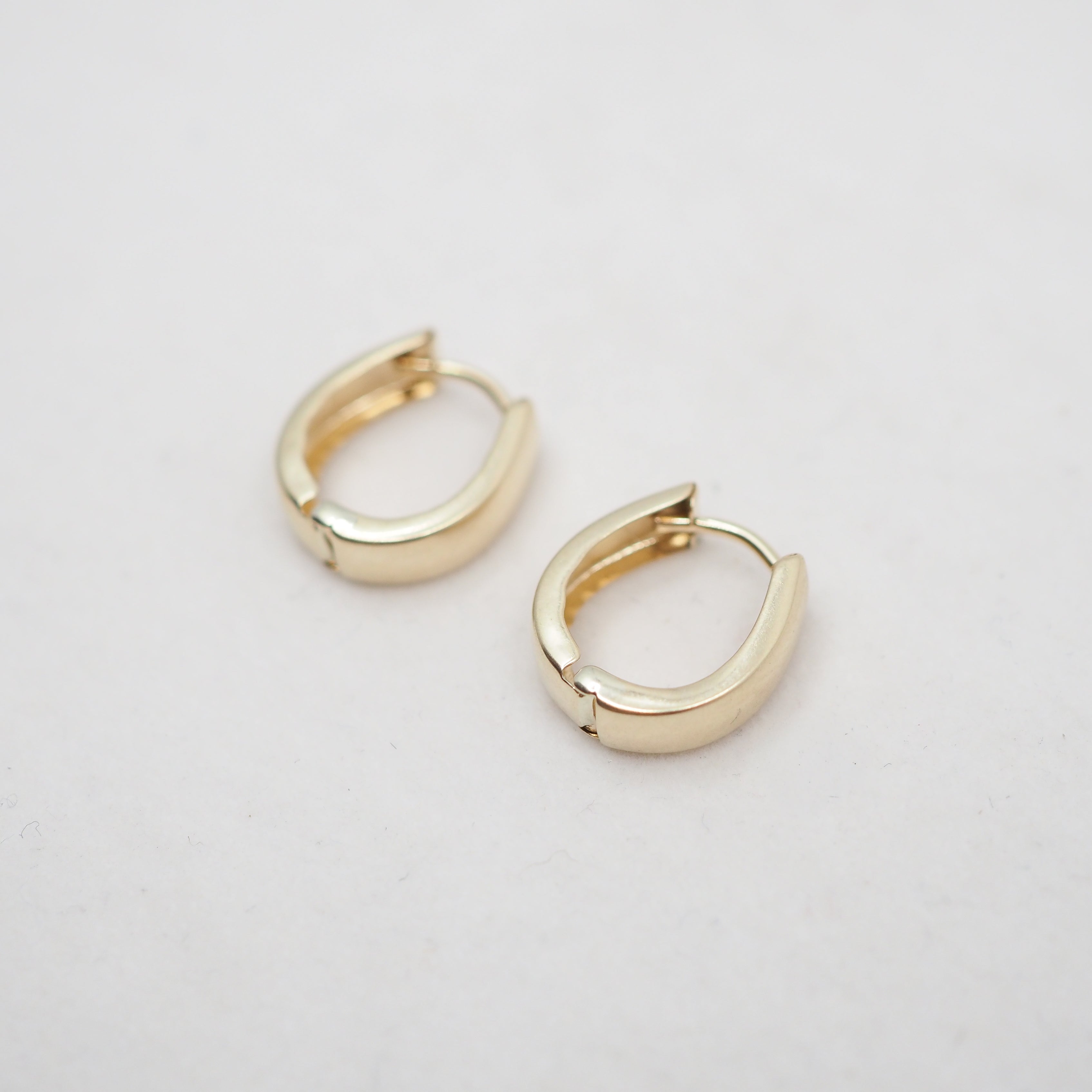 A close-up of a person's ear wearing a small, slim gold hoop earring.