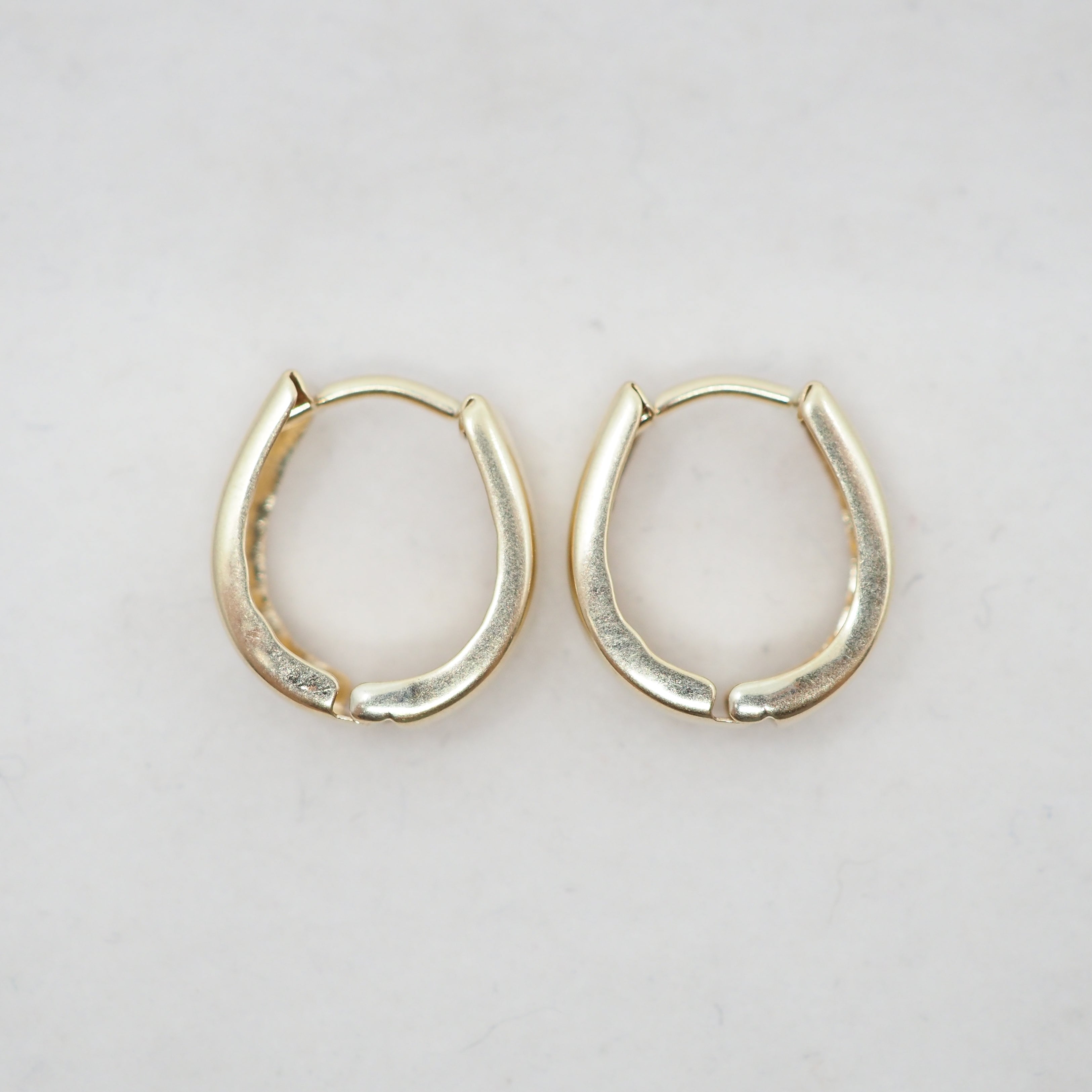 A pair of small gold huggie hoop earrings with a textured, matte finish, displayed on a light off-white background.