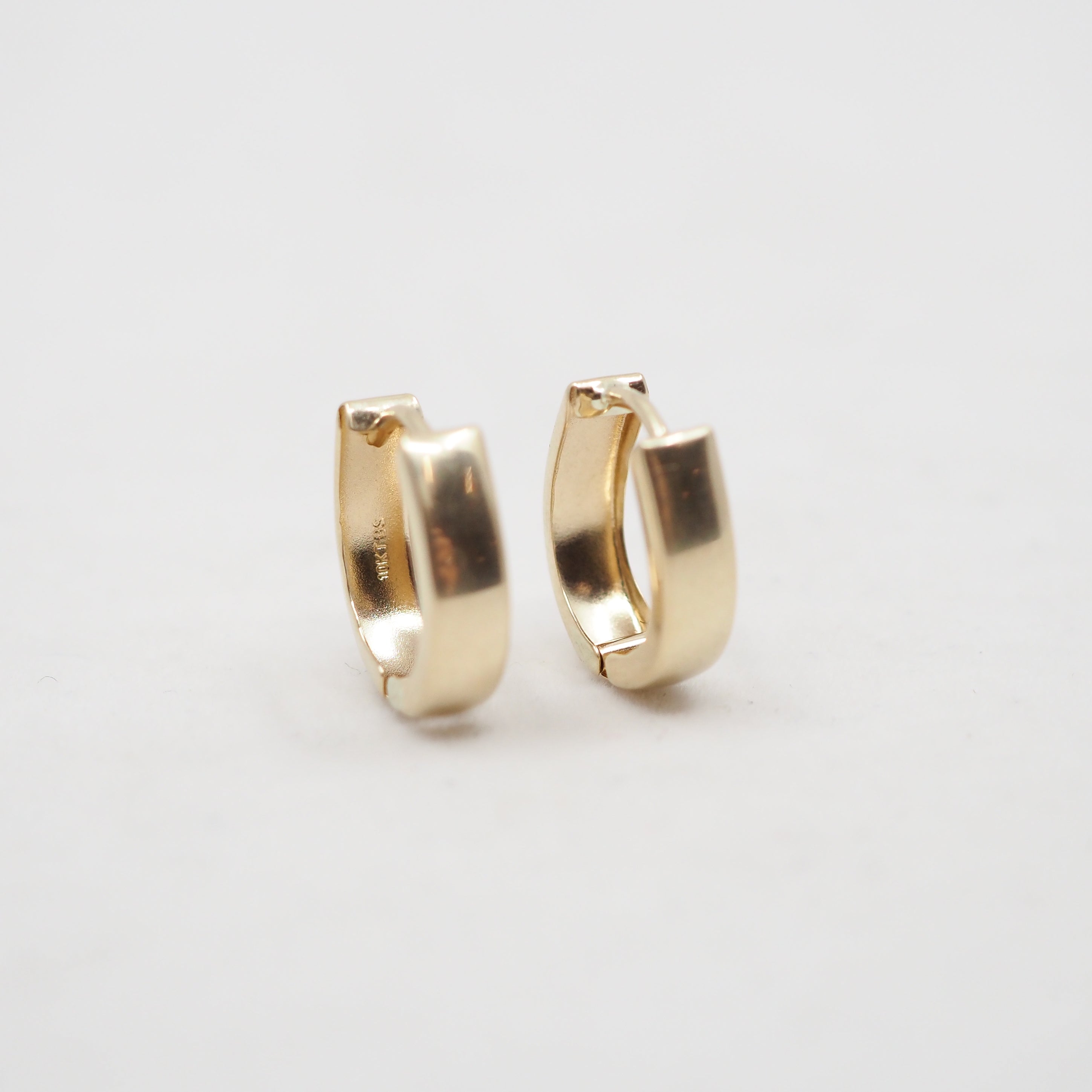 A pair of polished gold huggie hoop earrings on a clean, light gray background.