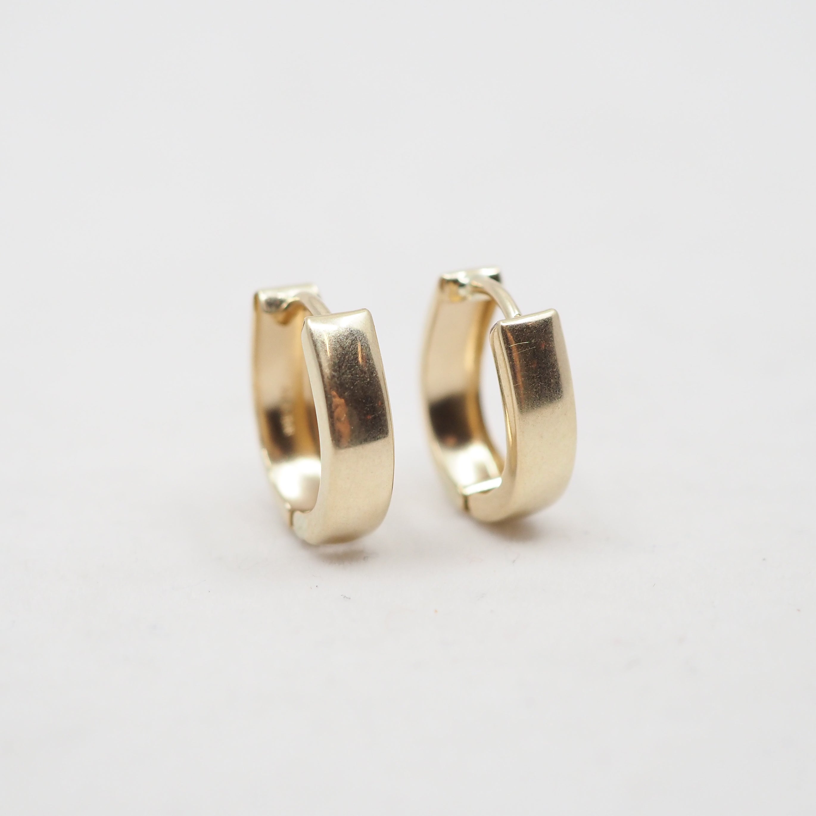 A pair of small gold huggie hoop earrings with a polished finish, displayed on a clean white background.