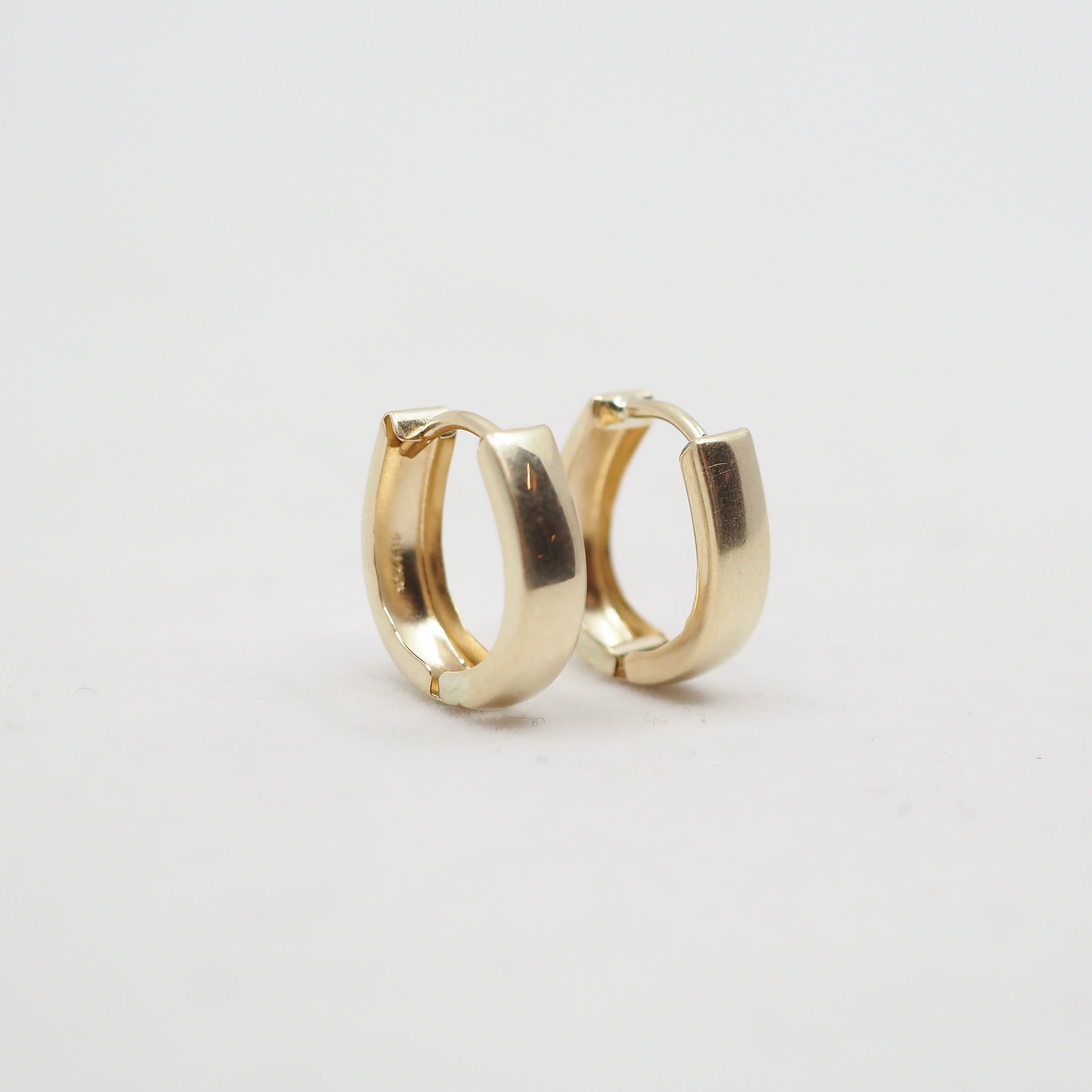 A pair of polished gold huggie hoop earrings on a clean, light off-white background.