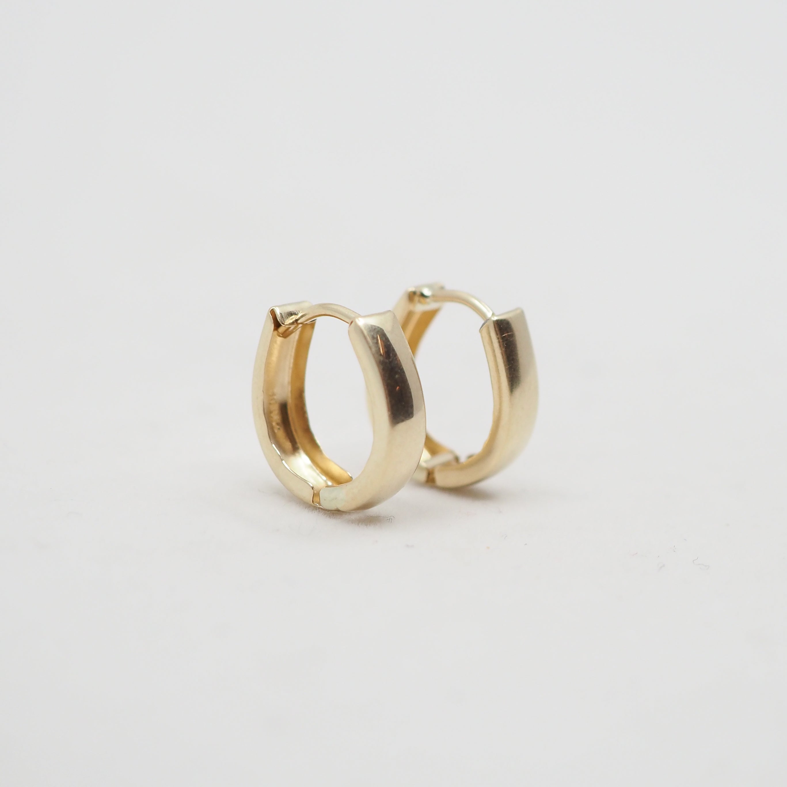 A close-up of a person's ear wearing a small, polished gold hoop earring.