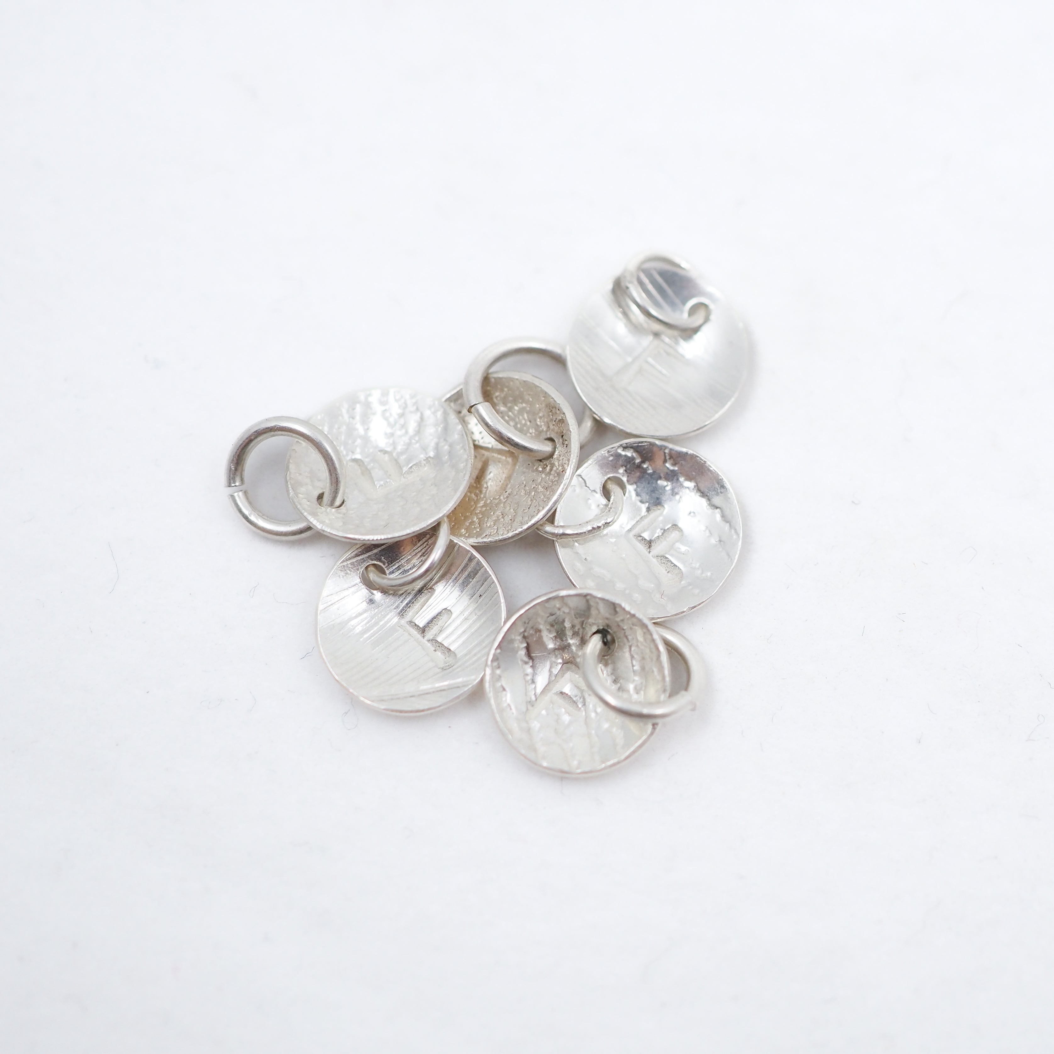 A cluster of hammered silver disc with the letter F charms with attached jump rings, displayed on a clean white background.